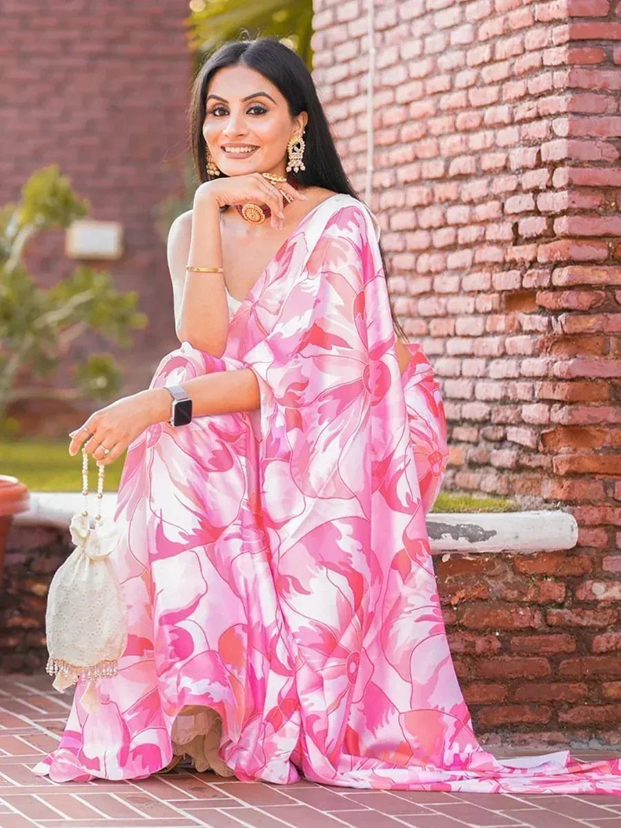 Woman in pink floral ethnic gown with gold jewelry, sitting by brick wall