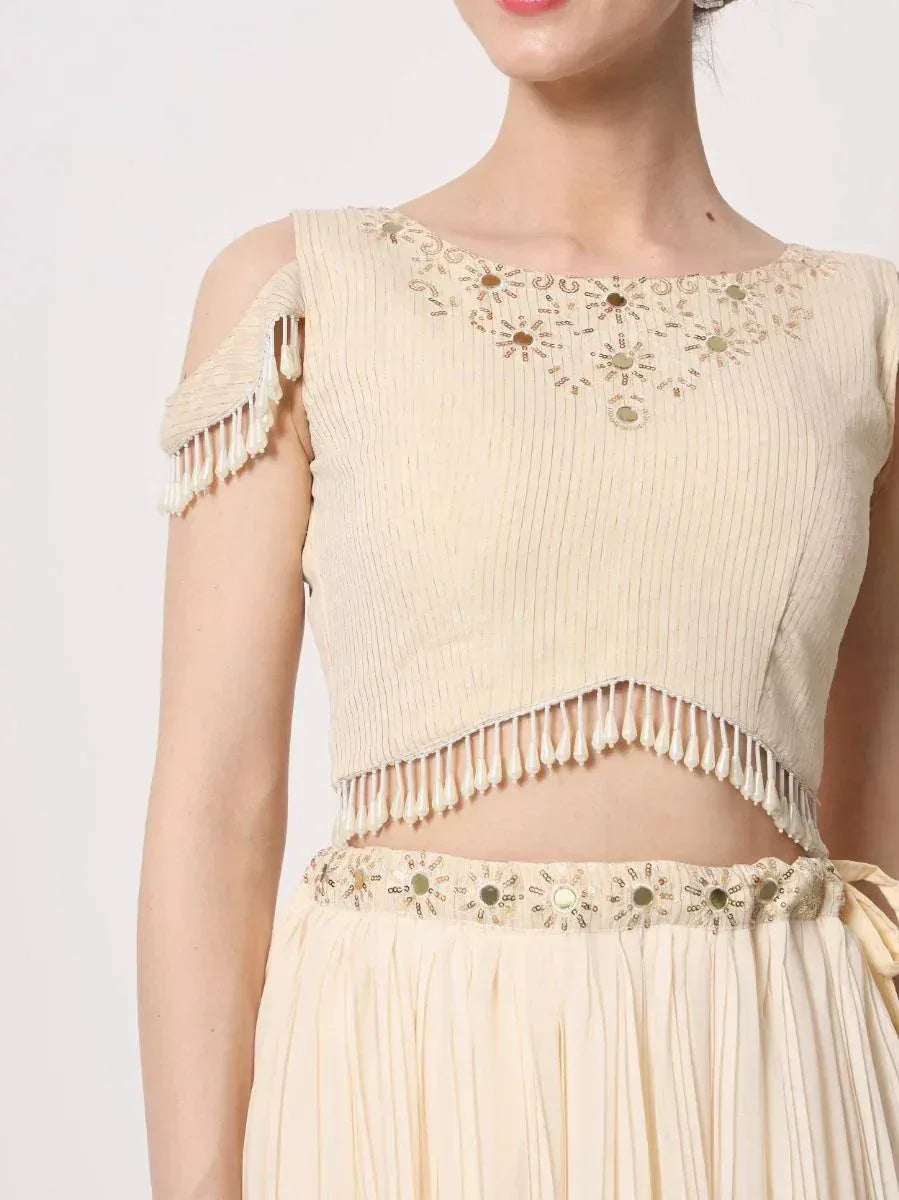Cream ethnic crop top with mirror work and tassels, paired with matching pleated skirt