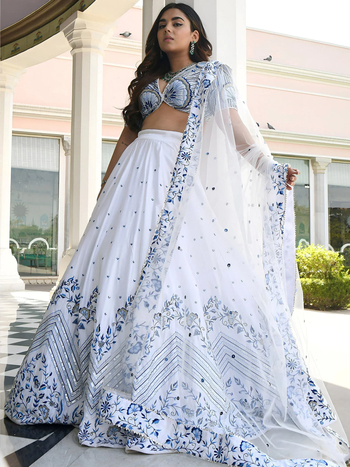 Woman wearing a white designer lehenga choli with blue floral embroidery and a matching dupatta
