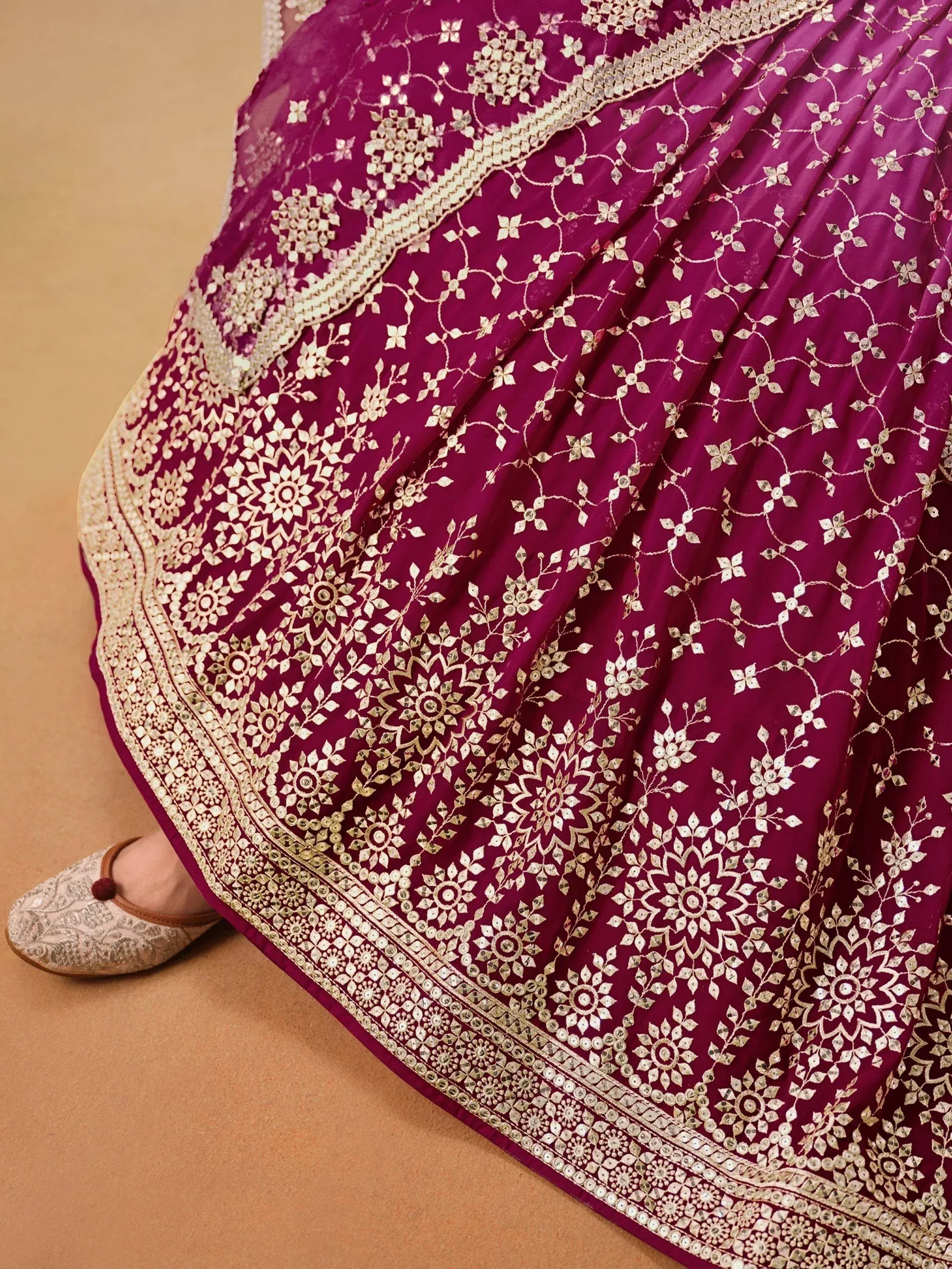 Magenta lehenga with gold floral embroidery and mirror work, paired with embellished flats