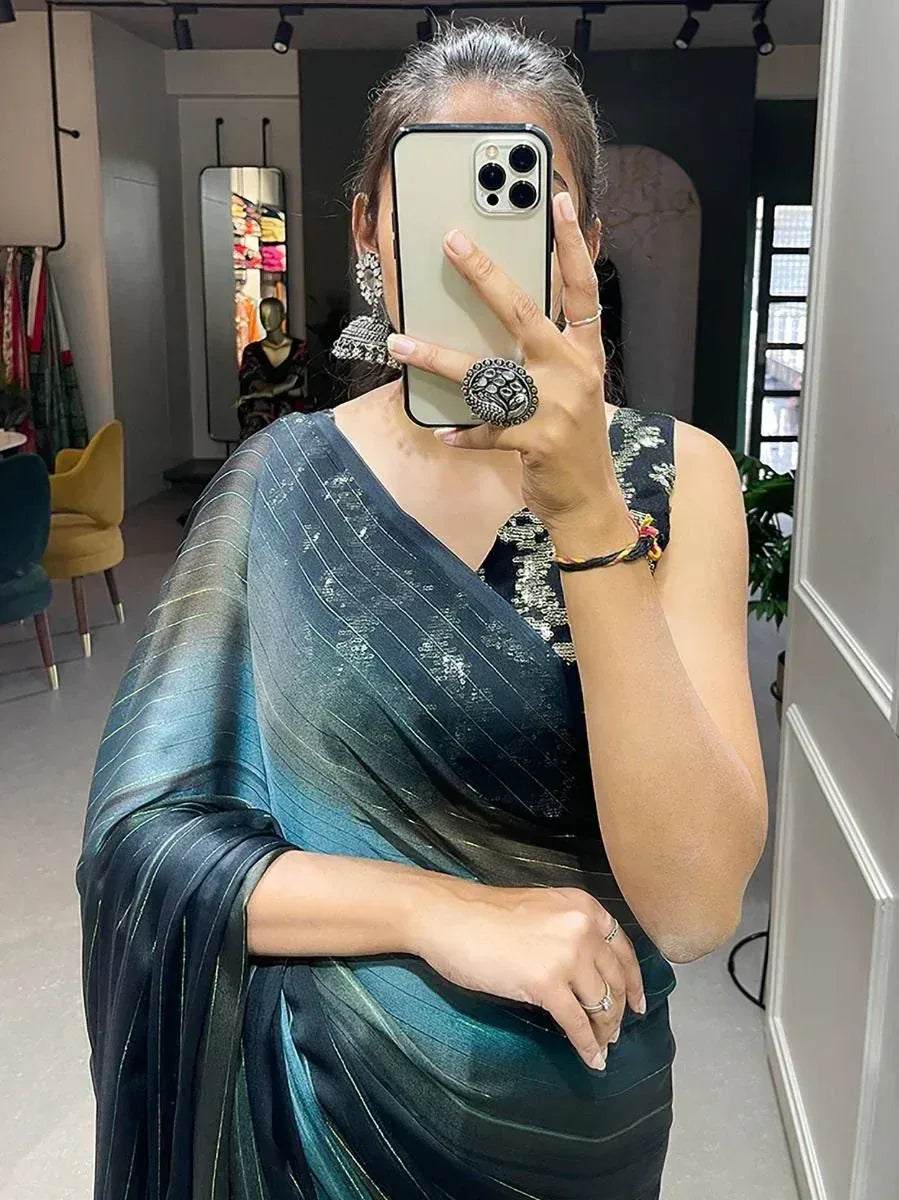 Woman in teal ombre saree with gold stripes, taking mirror selfie in boutique