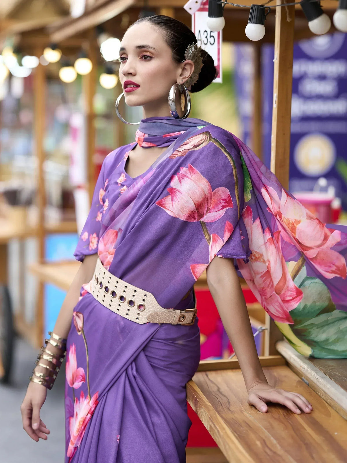 Purple floral saree with pink lotus print, styled with belt and hoop earrings for ethnic wear