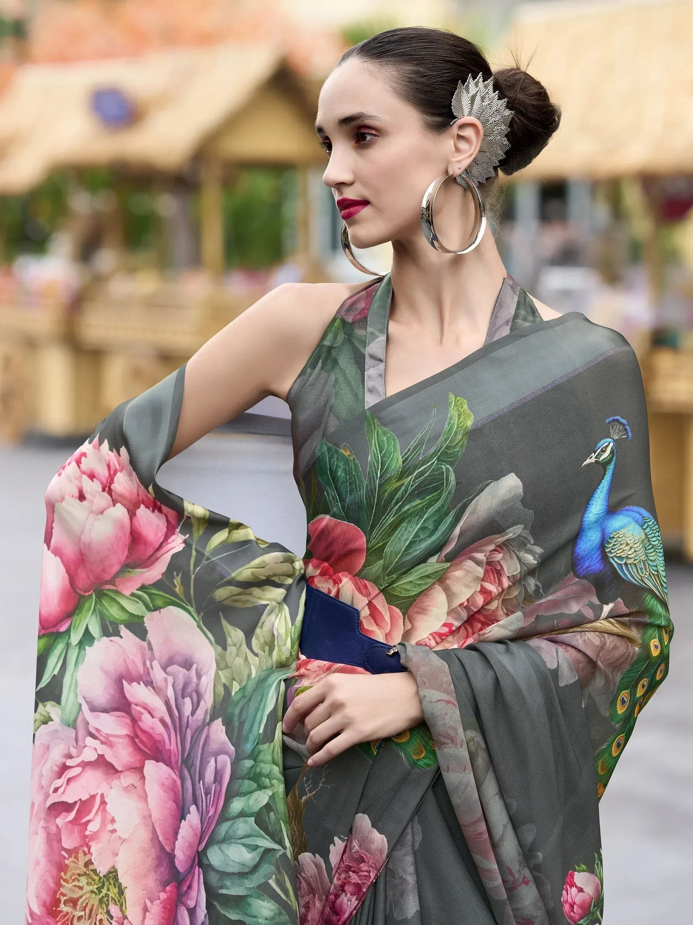 Woman in grey saree with peacock and floral print, styled with hoop earrings and leaf hair accessory