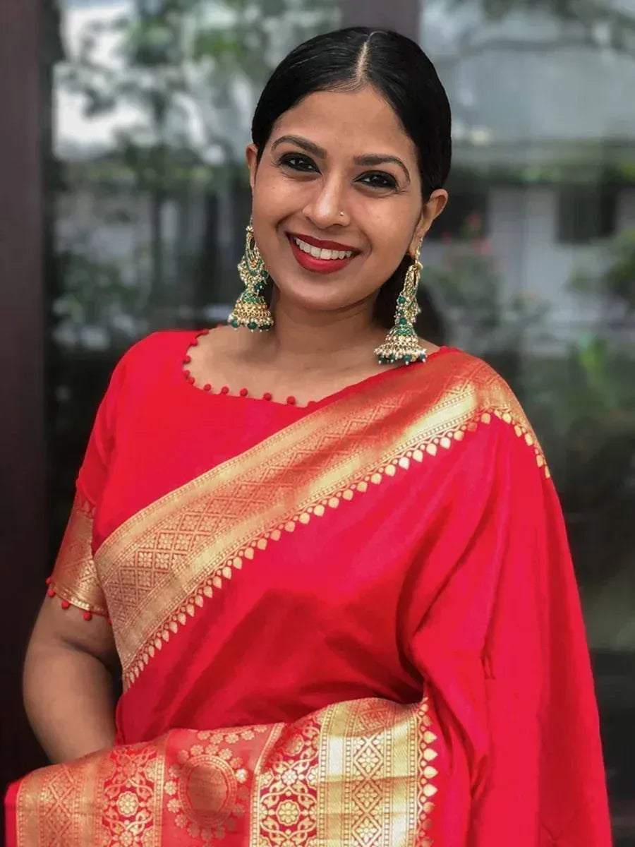 Woman in vibrant red Indian saree with gold zari border and matching blouse, styled with traditional jhumka earrings