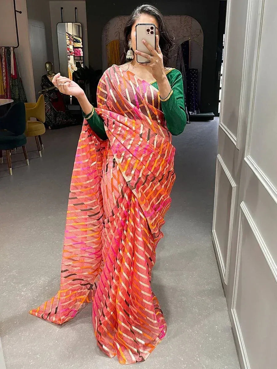 Woman wearing vibrant pink and orange printed saree with green blouse, taking mirror selfie in boutique