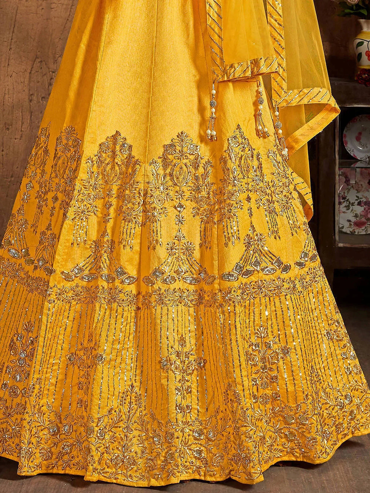 Close-up of a yellow designer lehenga with intricate gold zari embroidery and sequin work.