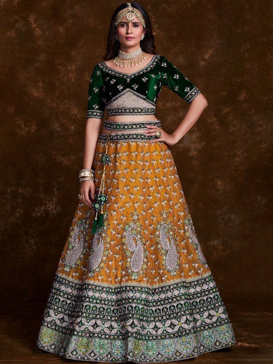 Green velvet and mustard yellow embroidered lehenga choli with heavy embellishments and traditional jewelry