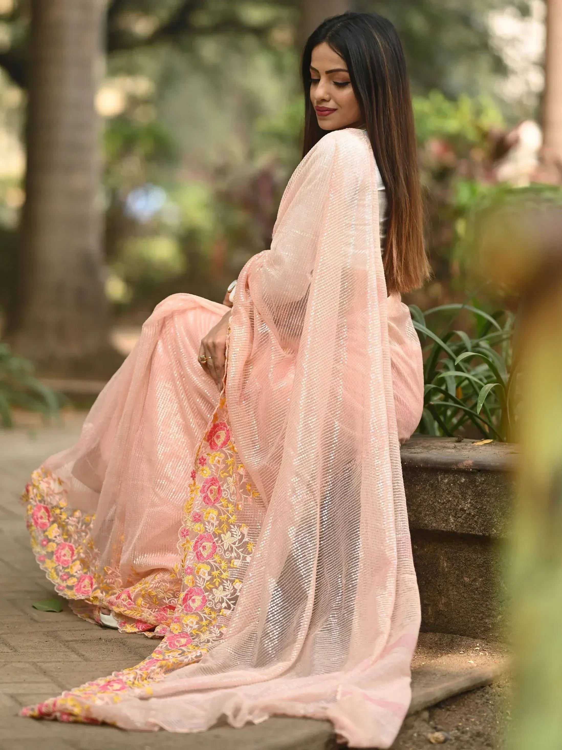Woman in pink embroidered ethnic gown with floral details, seated outdoors