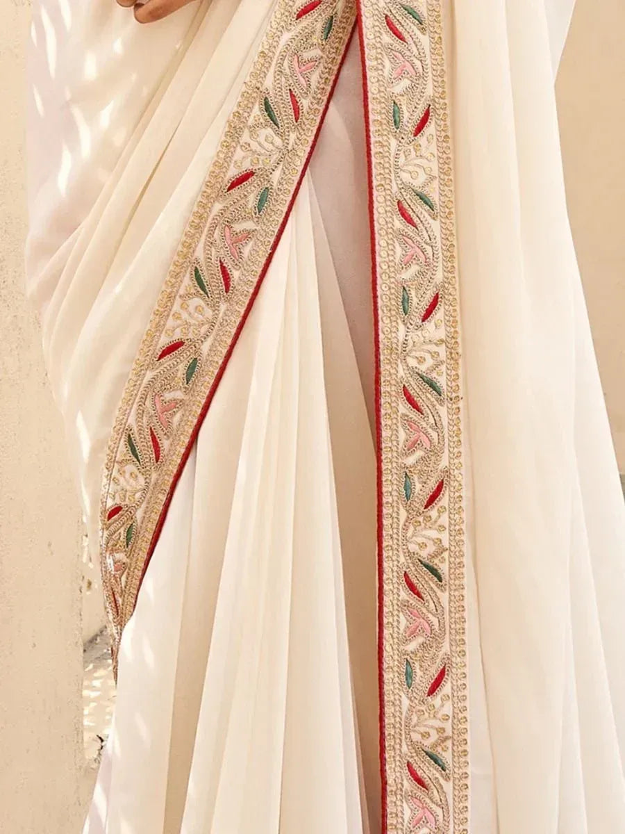 Cream saree with intricate gold, red, and green embroidery on border, elegant Indian ethnic wear