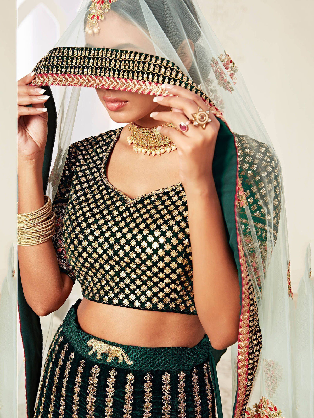 Emerald green designer lehenga choli with gold sequin work, sheer dupatta, and traditional Indian bridal jewelry