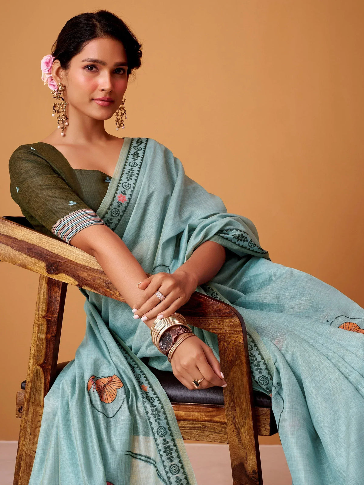 Woman in light blue embroidered saree with olive green blouse, floral hair accessory, and gold jewelry