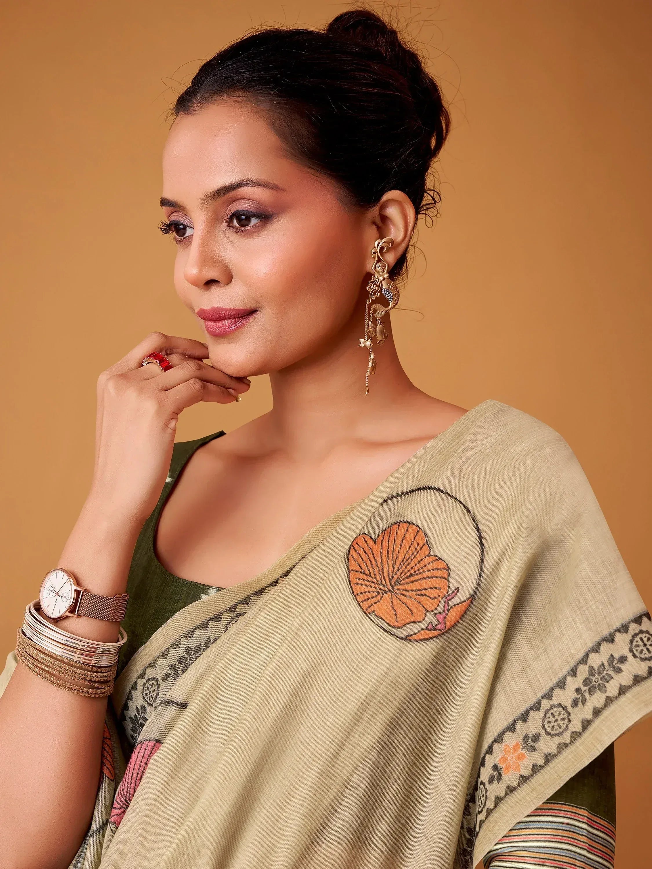 Woman in beige saree with floral embroidery, gold earrings, and green blouse, styled for Indian ethnic wear