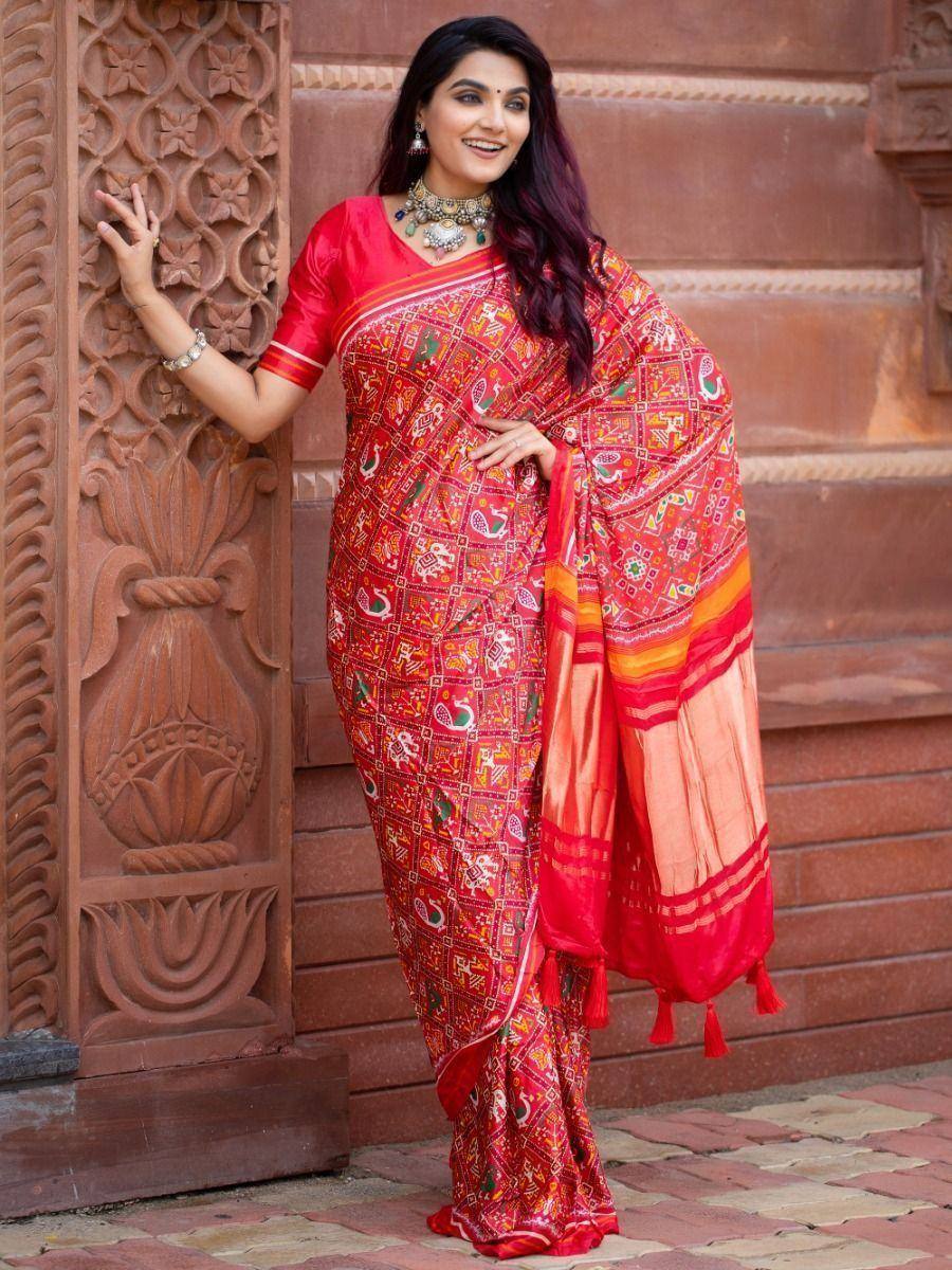 Red printed ethnic saree with peacock motifs, paired with blouse, worn against carved stone backdrop