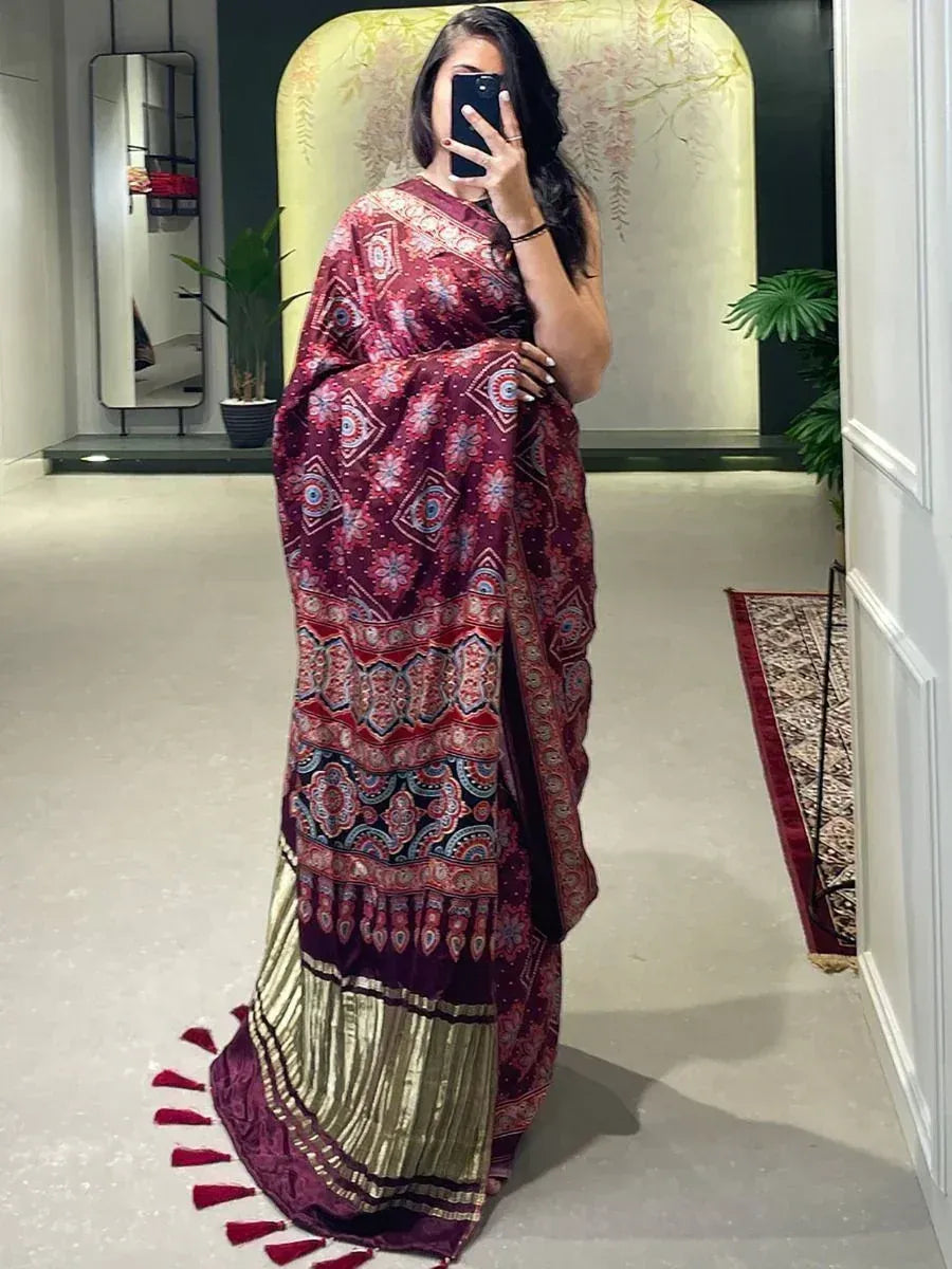Elegant maroon saree with intricate paisley and geometric patterns, gold border, and tassels, perfect for ethnic occasions.
