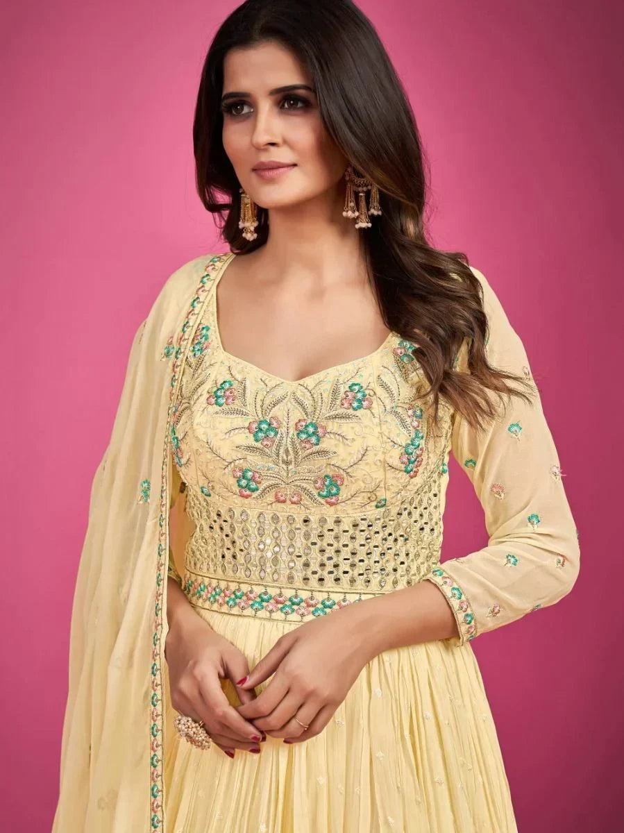 Woman wearing yellow embroidered Indian ethnic gown with floral details, pink background