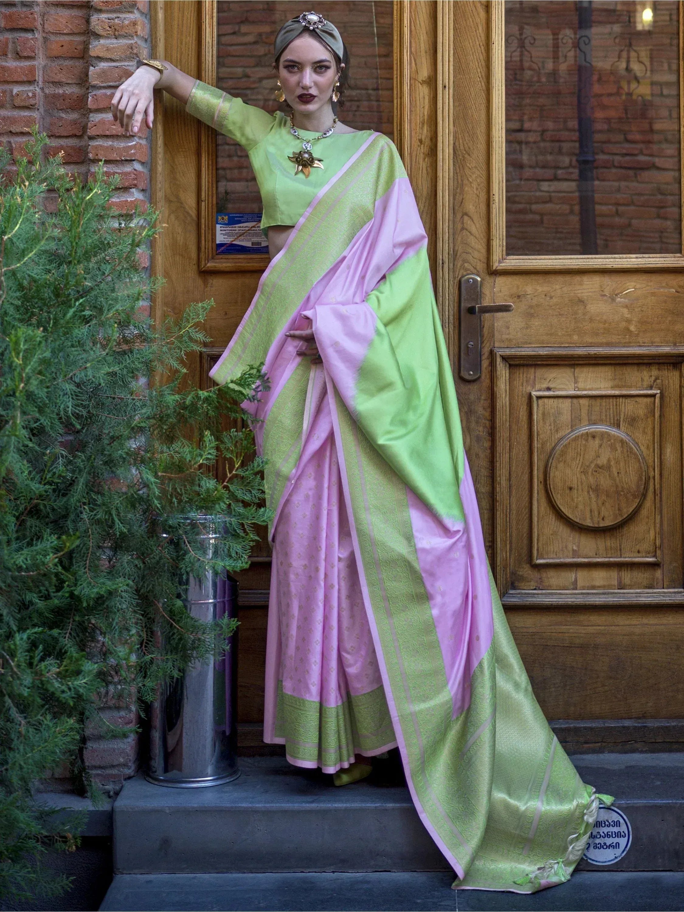 Woman in pink and green designer saree with matching blouse, ethnic jewelry, standing by wooden door
