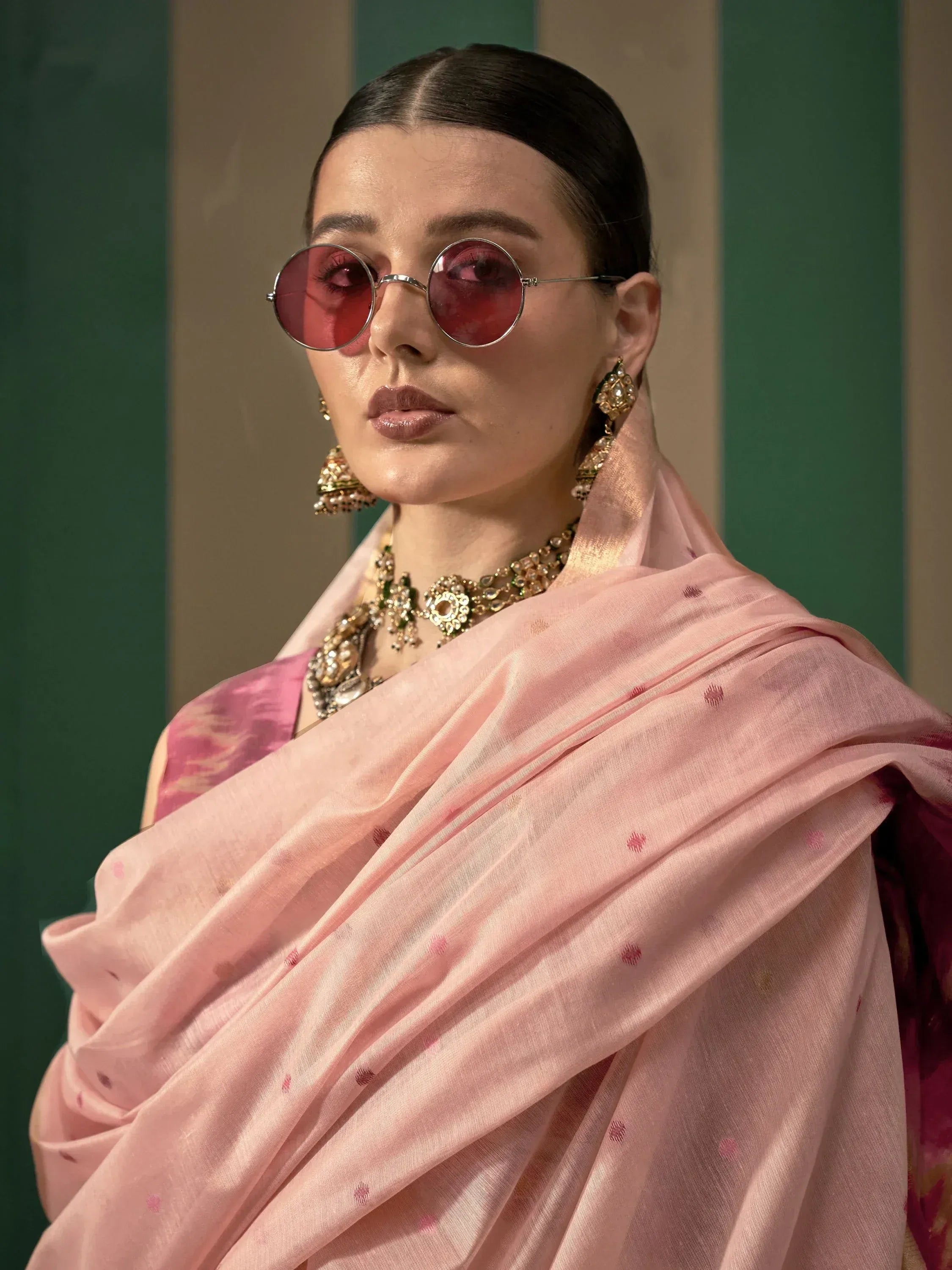 Woman in pink ethnic saree with gold jewelry and round sunglasses, styled for Indian fashion