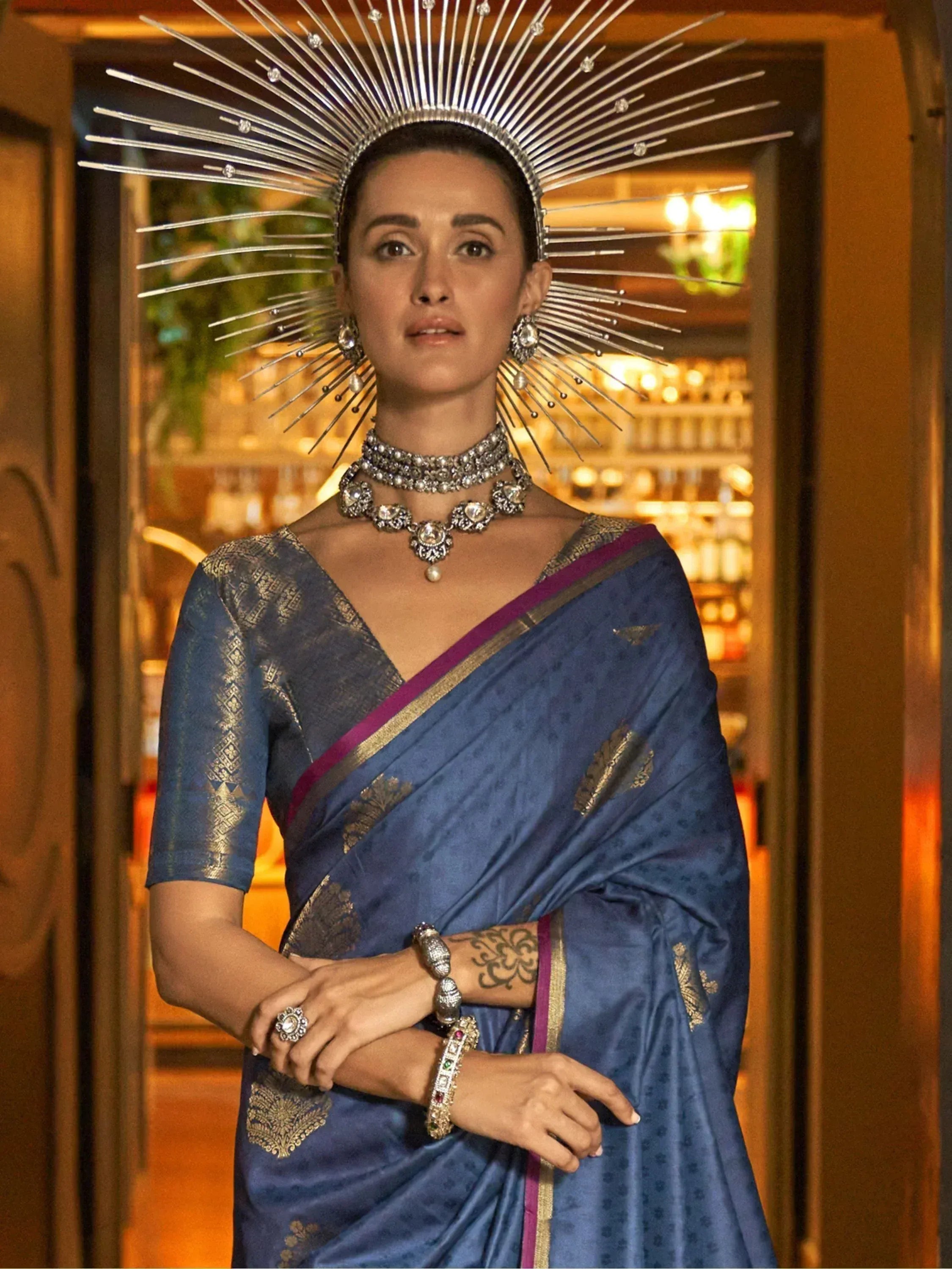 Woman in blue designer saree with gold embroidery, statement jewelry, and dramatic sunburst headpiece