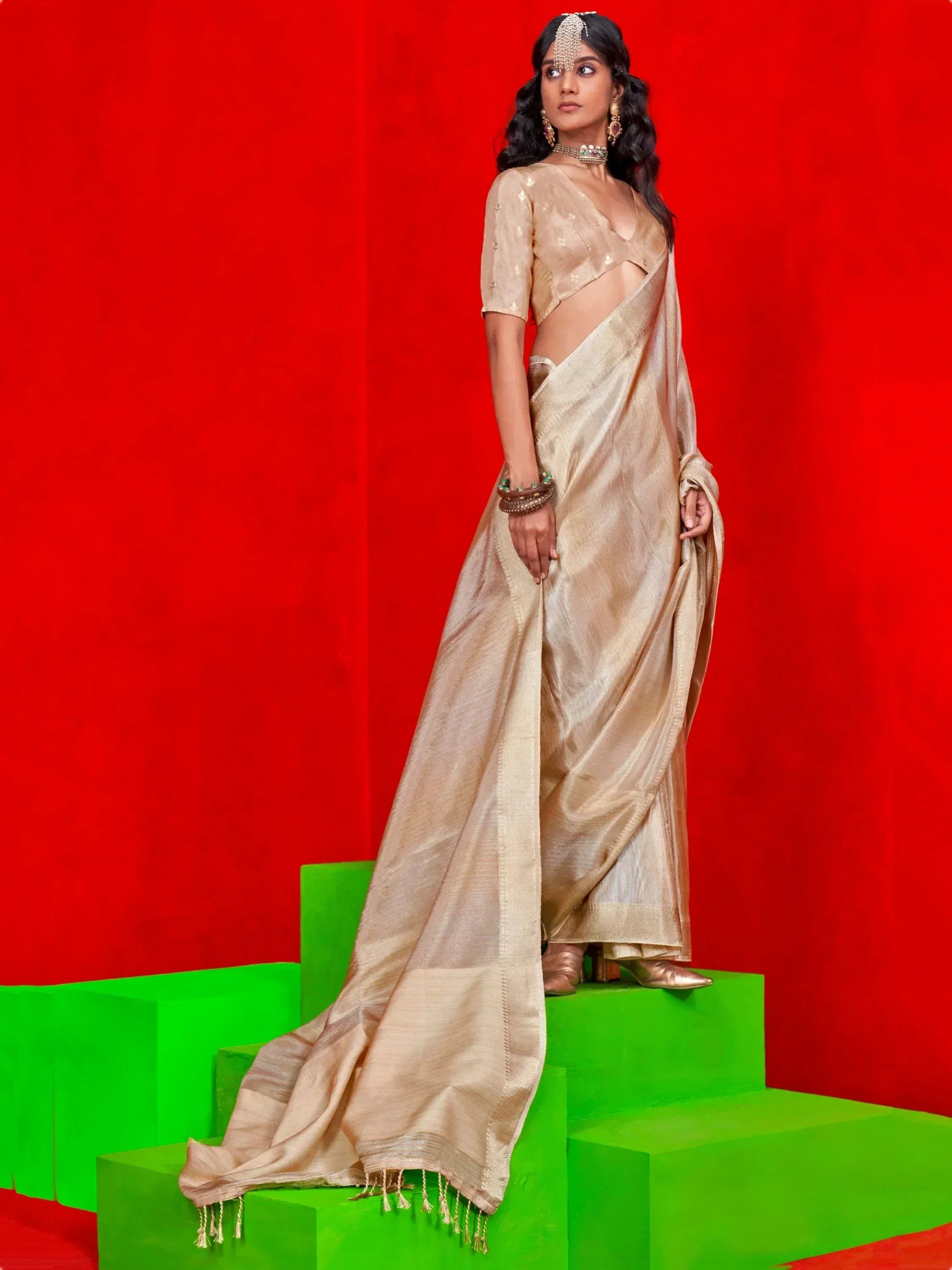 Elegant gold saree with matching blouse, traditional Indian ethnic wear for women, styled with jewelry on green steps against red backdrop