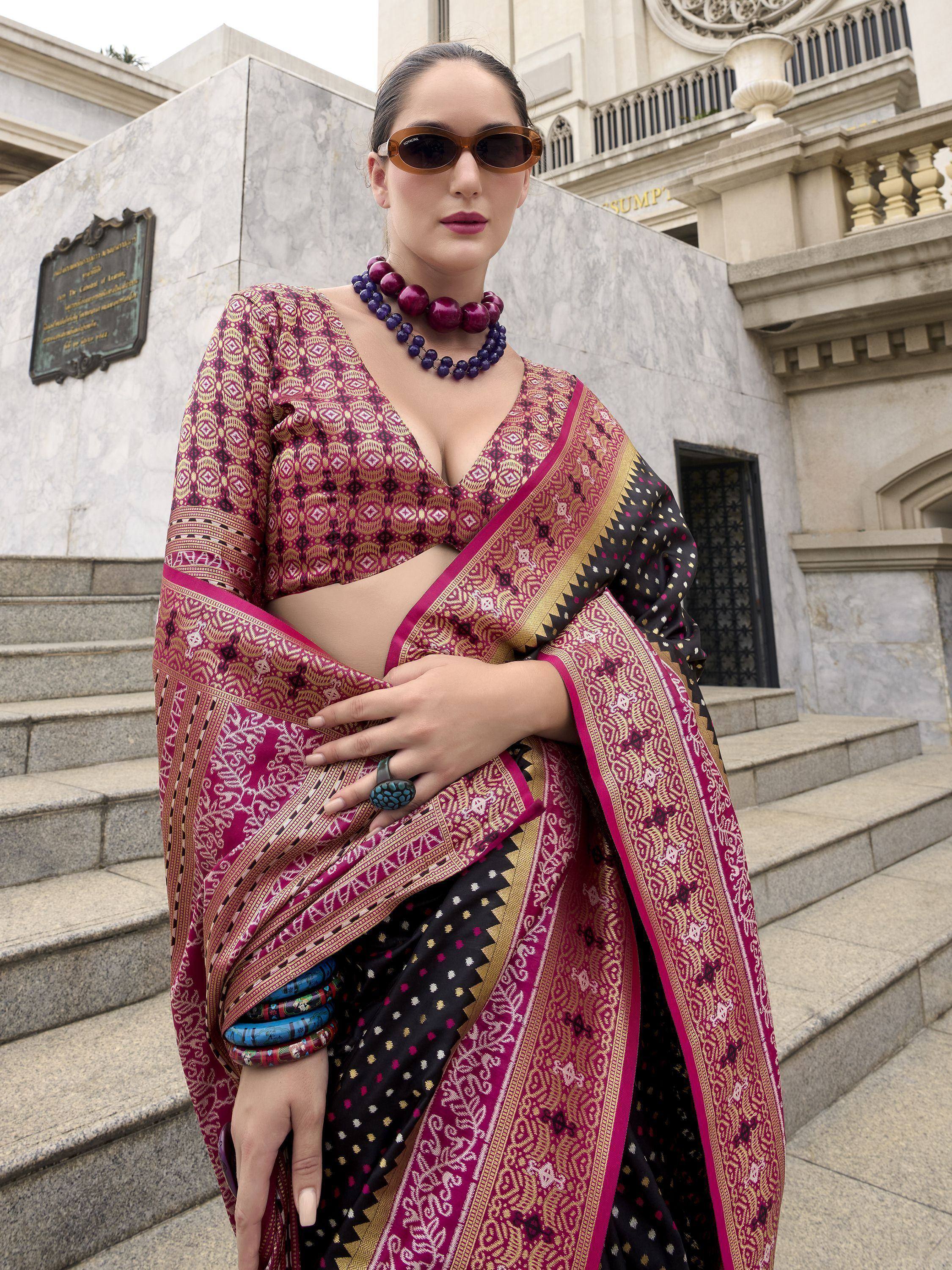 Woman in maroon and black designer saree with gold patterns, styled with statement jewelry and sunglasses.