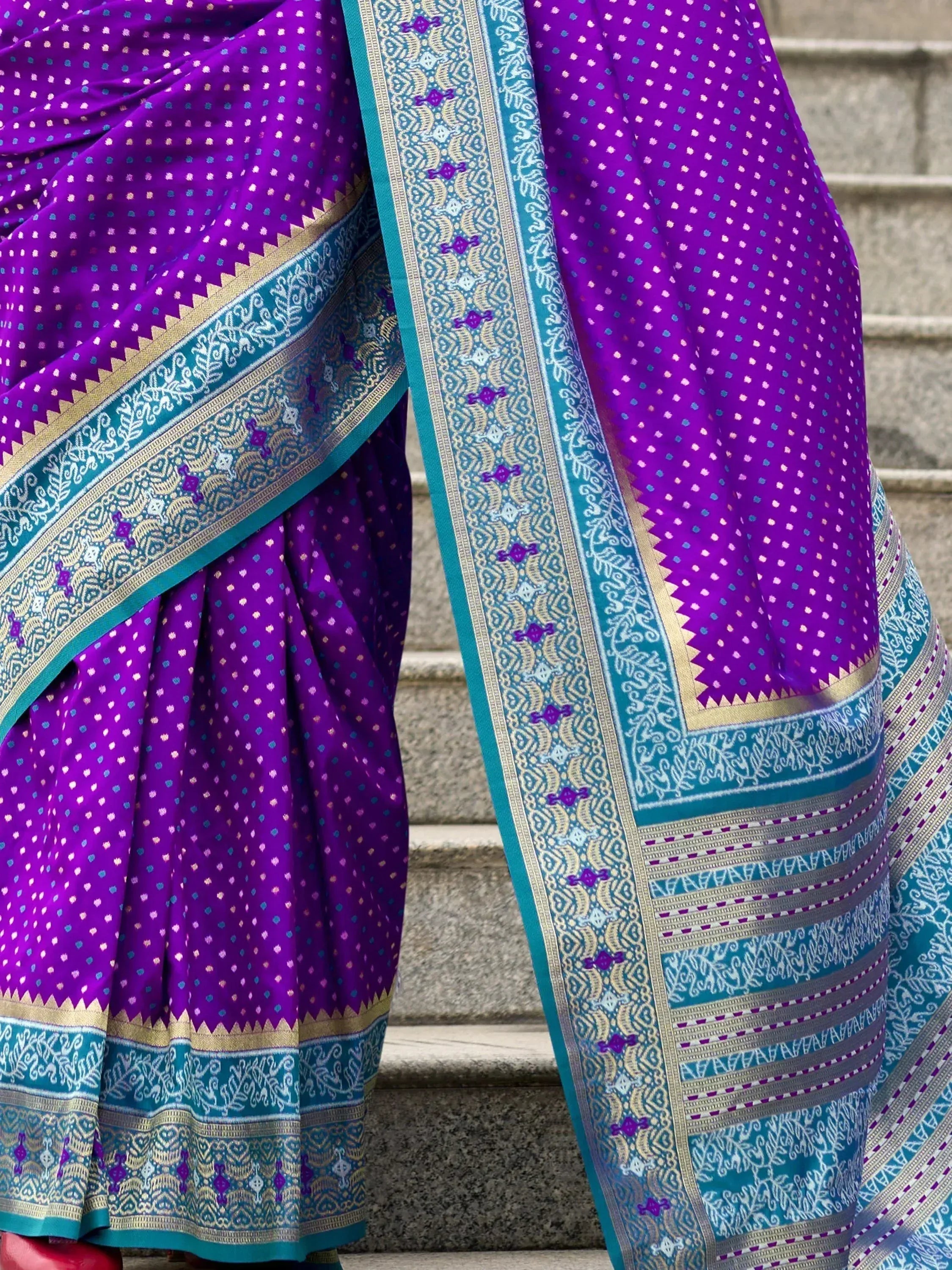 Purple ethnic saree with turquoise border, intricate gold zari work, and dotted pattern, perfect for Indian occasions.