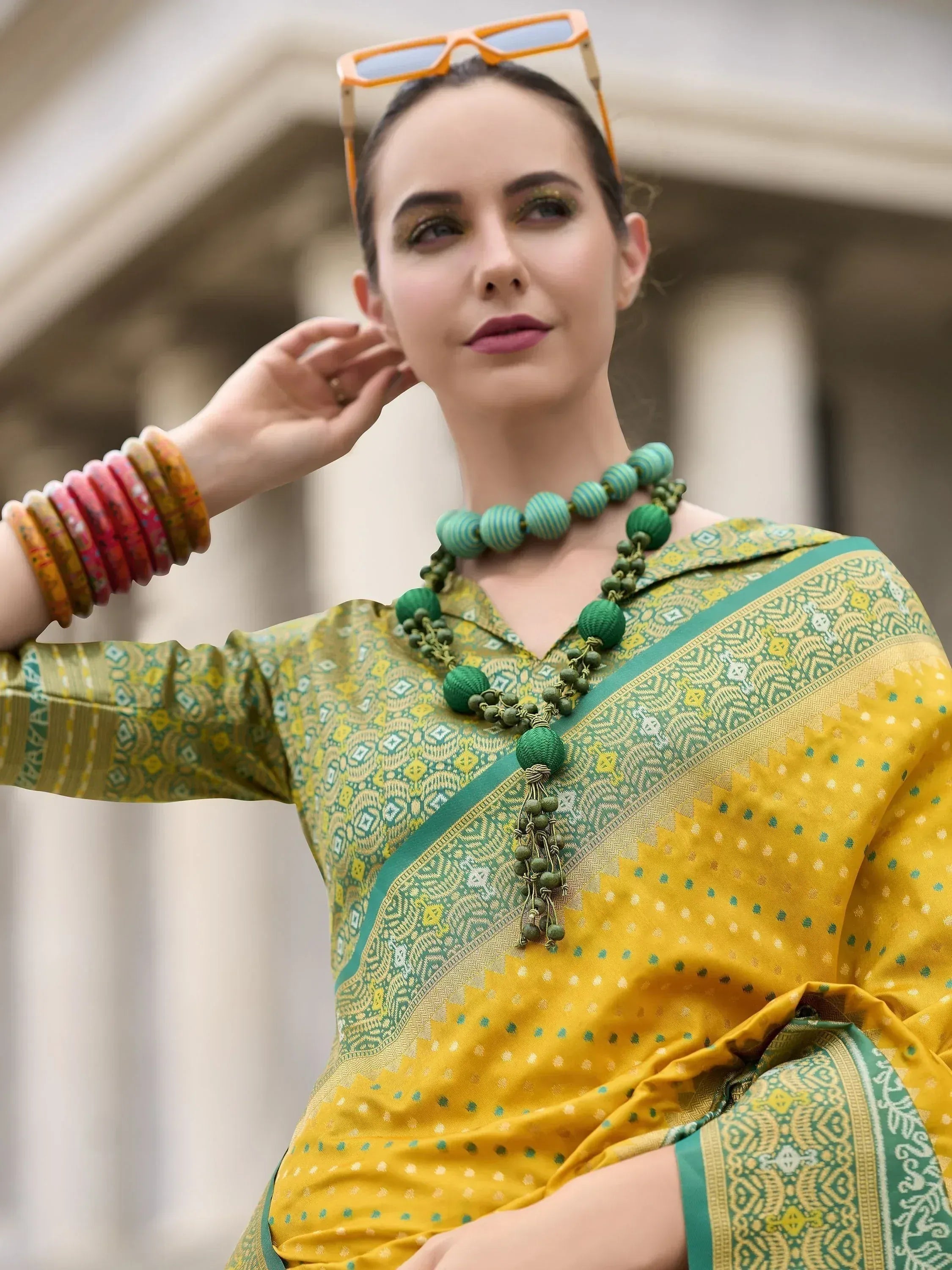 Woman in vibrant yellow and green ethnic saree with patterned blouse, colorful bangles, and statement necklace