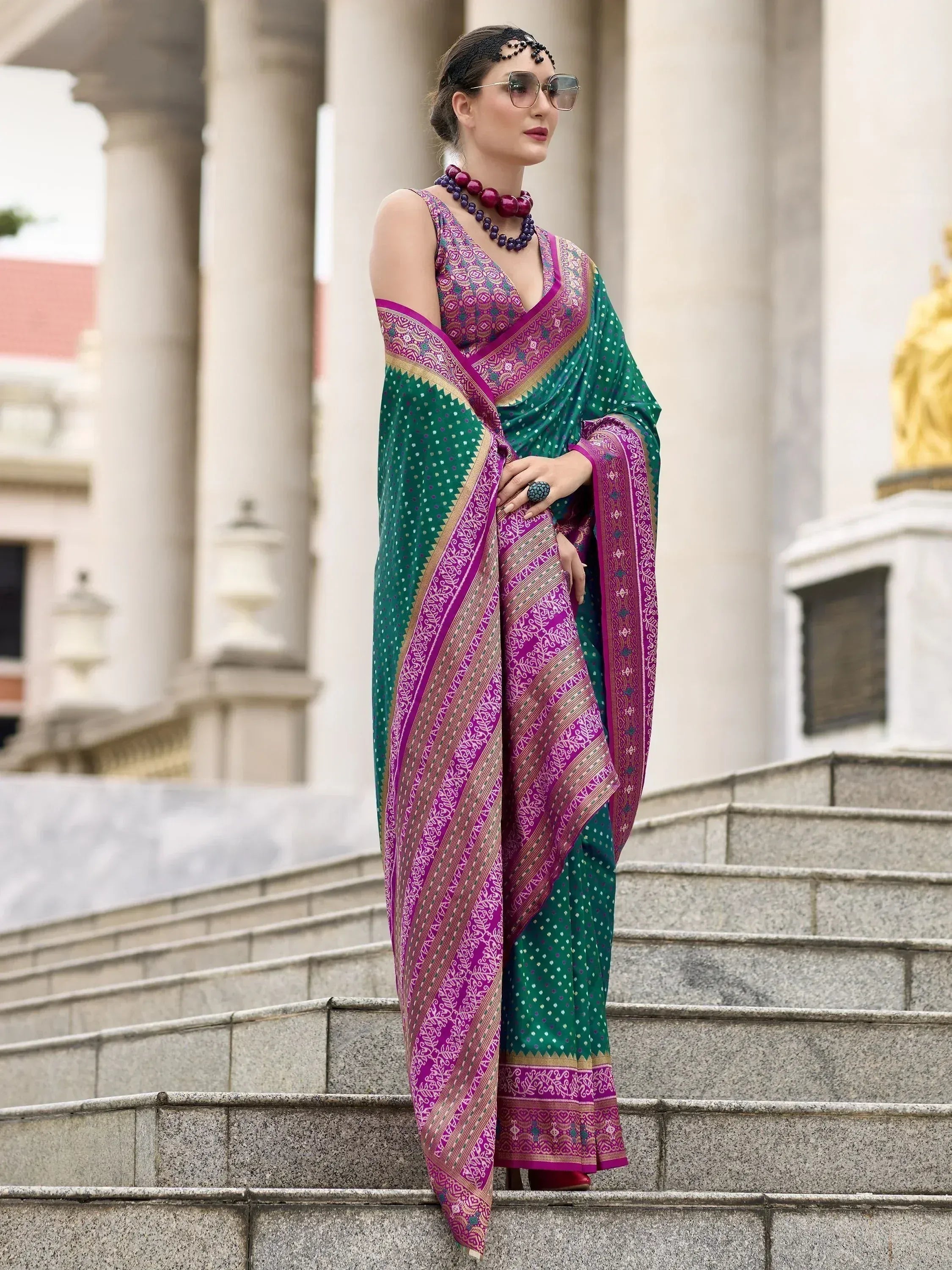 Woman in green and magenta ethnic saree with intricate patterns, styled with statement jewelry on stone steps