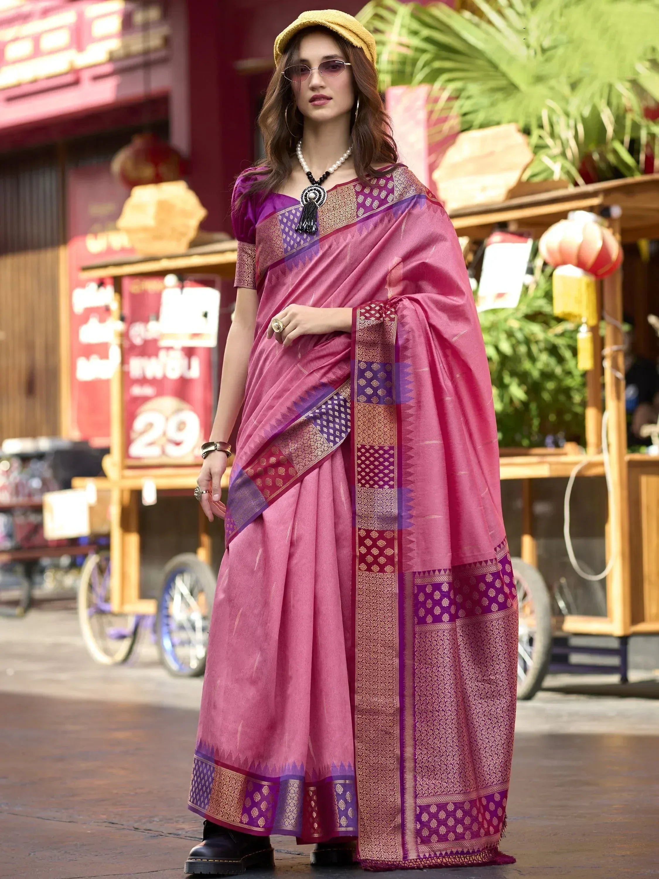 Woman in pink and purple designer saree with gold border, styled with yellow hat and boots for ethnic fashion