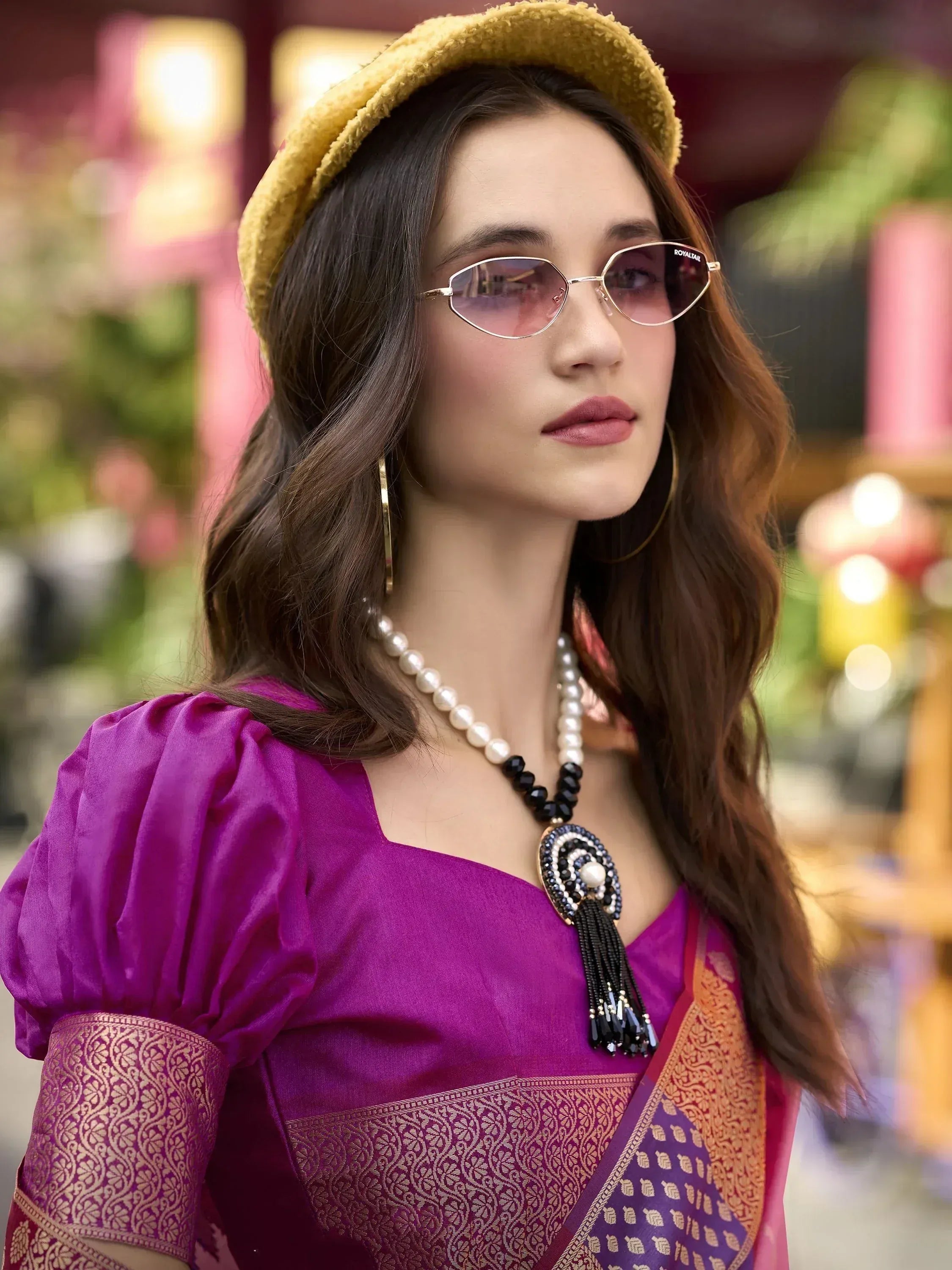 Woman in purple ethnic gown with gold embroidery, yellow hat, and statement necklace