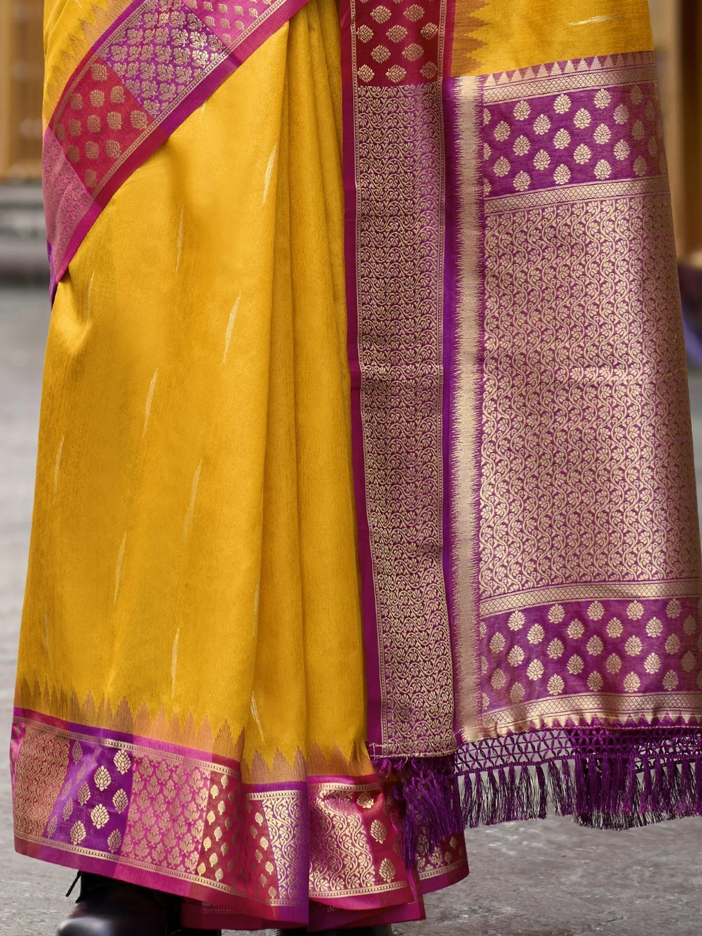 Yellow and purple designer saree with intricate gold zari work and tassels, perfect for ethnic occasions.