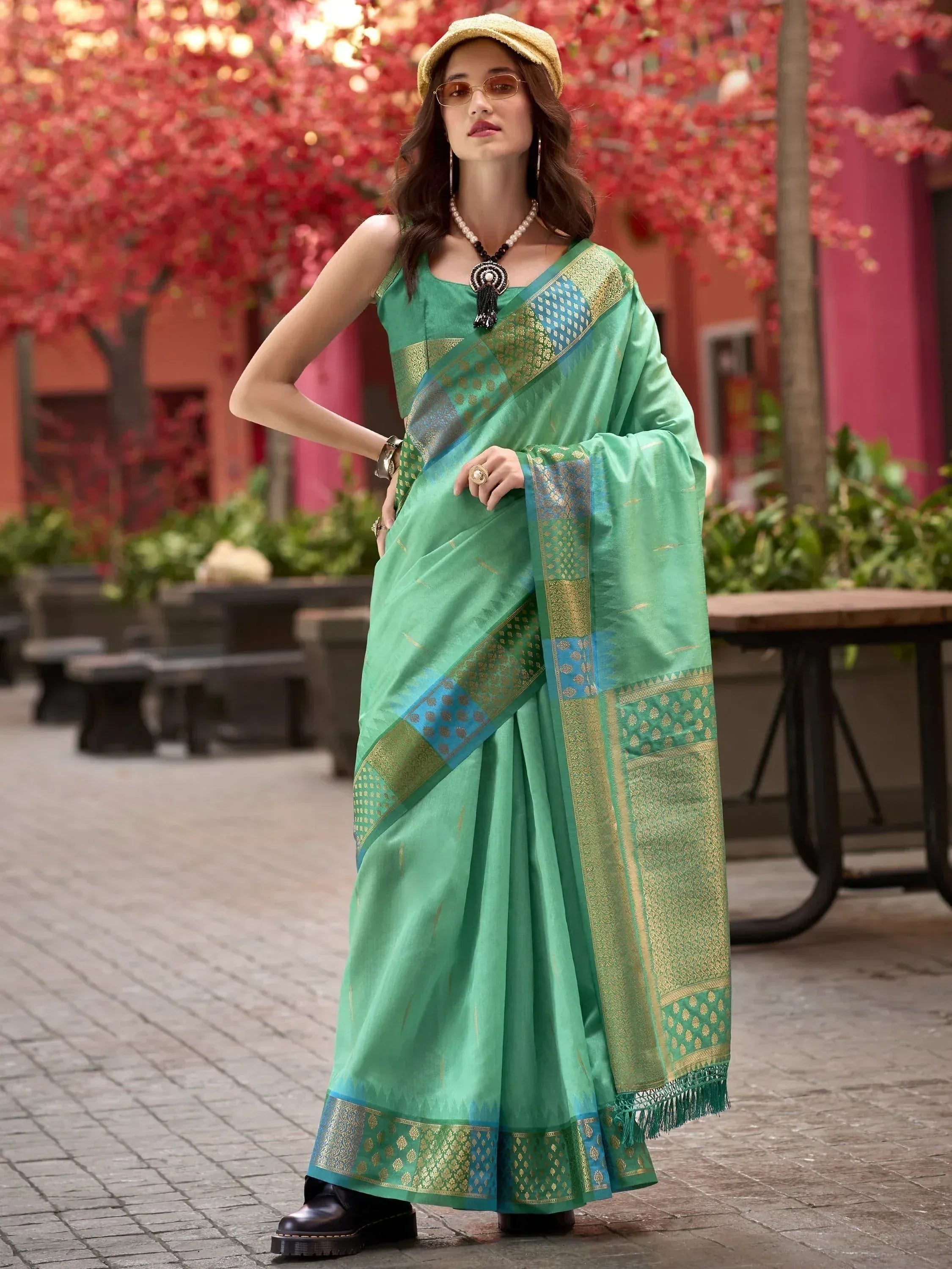 Green designer saree with gold and blue border, styled with hat and boots for ethnic fashion