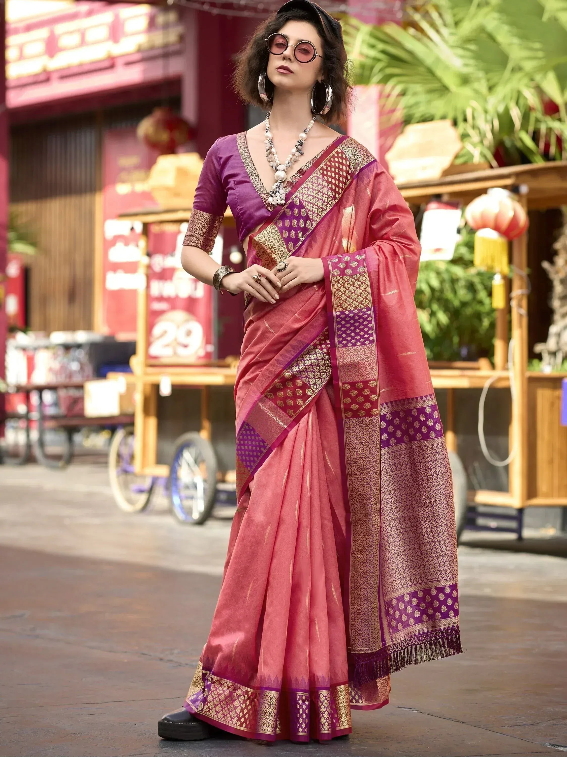 Woman in pink and purple designer saree with gold embroidery, styled with sunglasses and statement jewelry