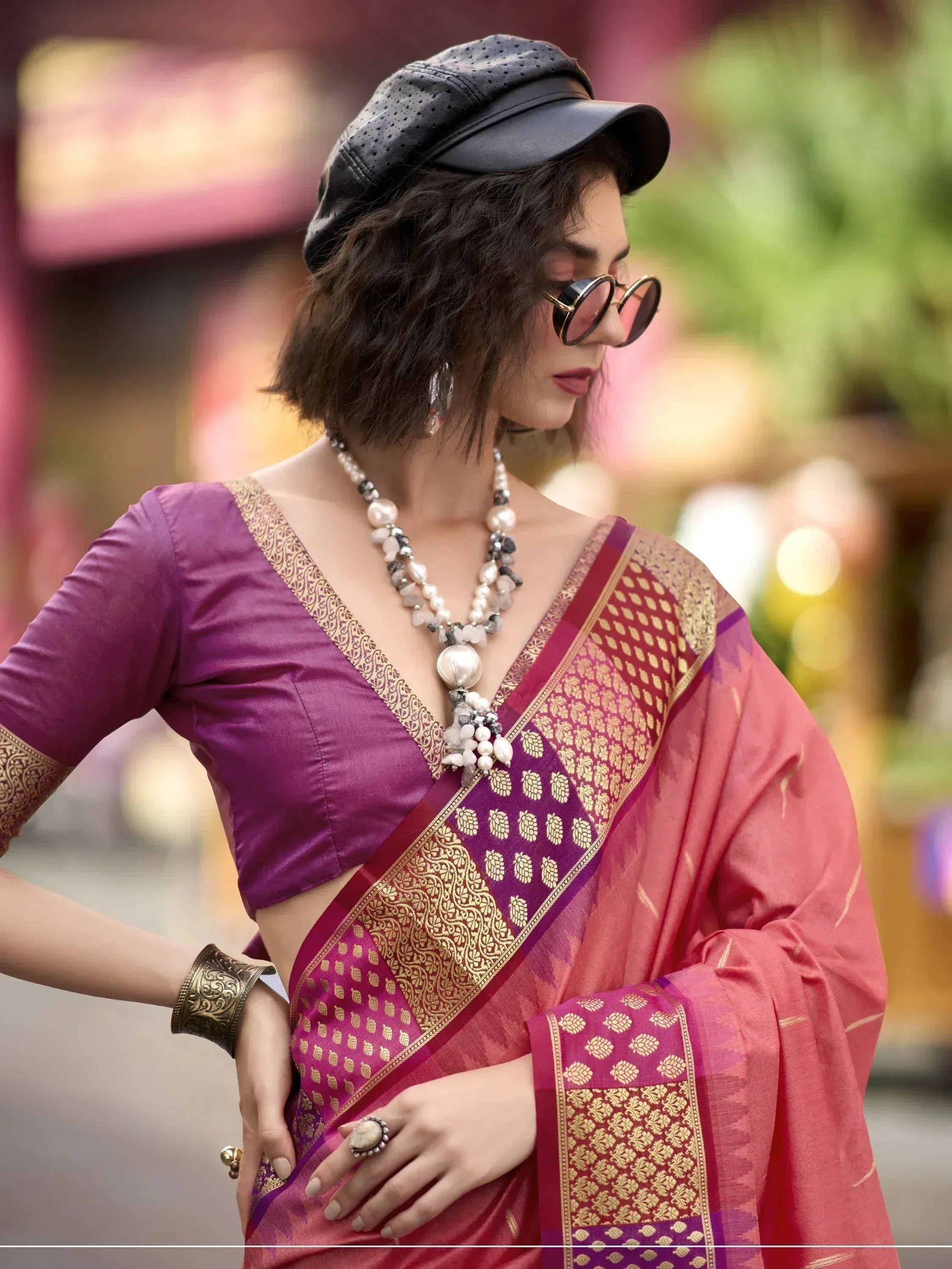 Woman in purple and pink ethnic saree with gold border, black cap, and statement jewelry