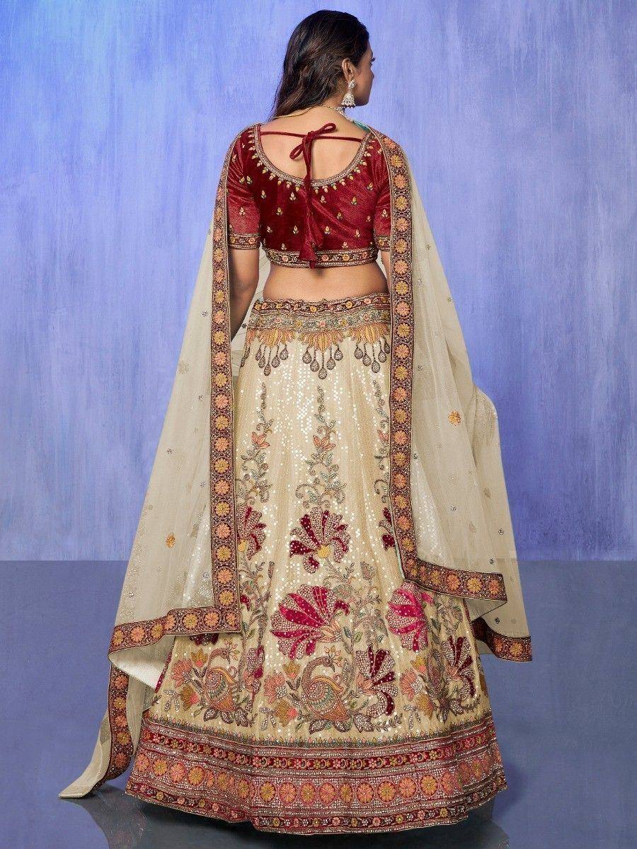 Back view of woman in embroidered beige lehenga choli with maroon velvet blouse and floral dupatta