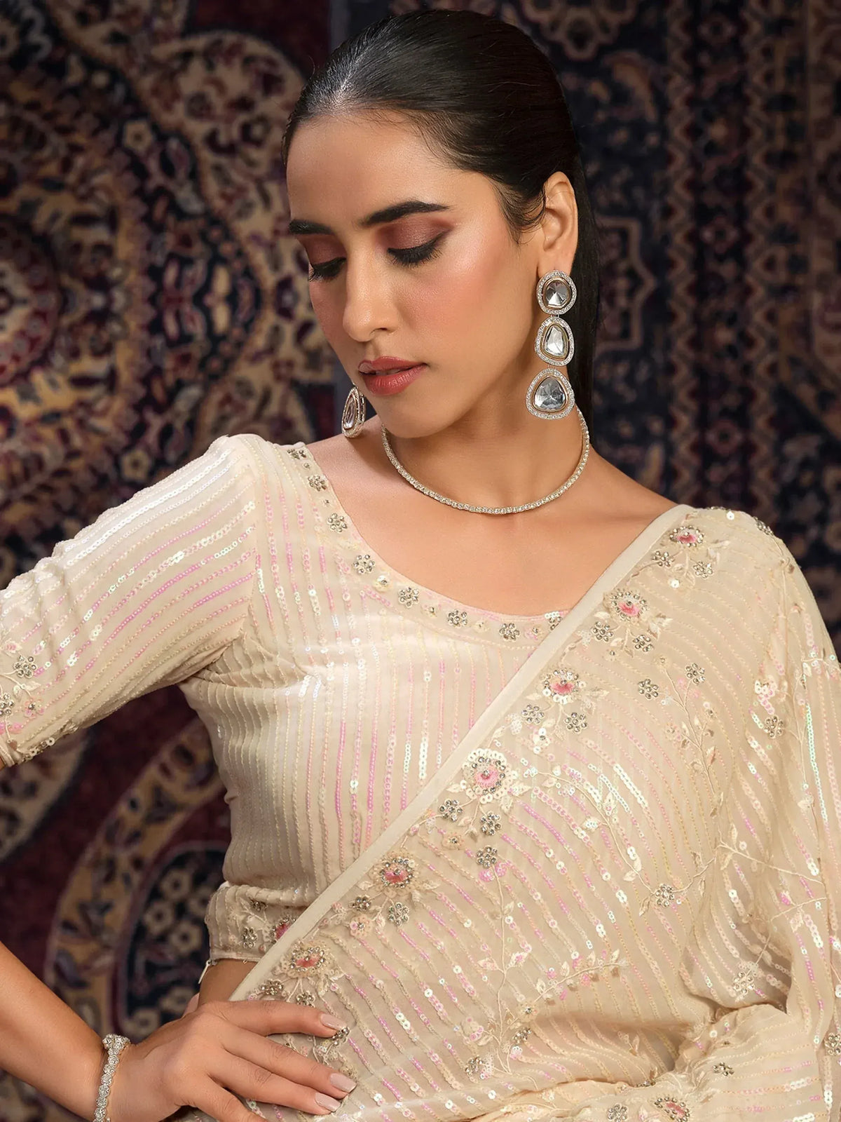 Elegant cream saree with pink sequin stripes and floral embroidery, paired with statement earrings for Indian ethnic wear.