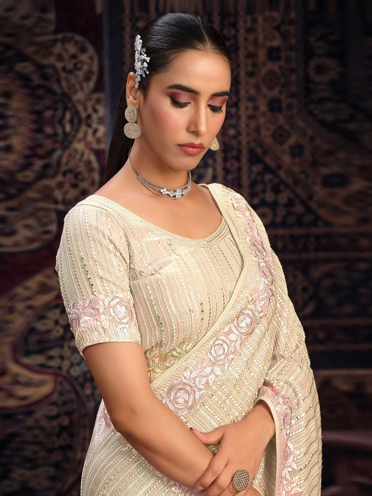 Elegant cream saree with pink floral embroidery and sequin work, paired with statement jewelry for festive occasions.
