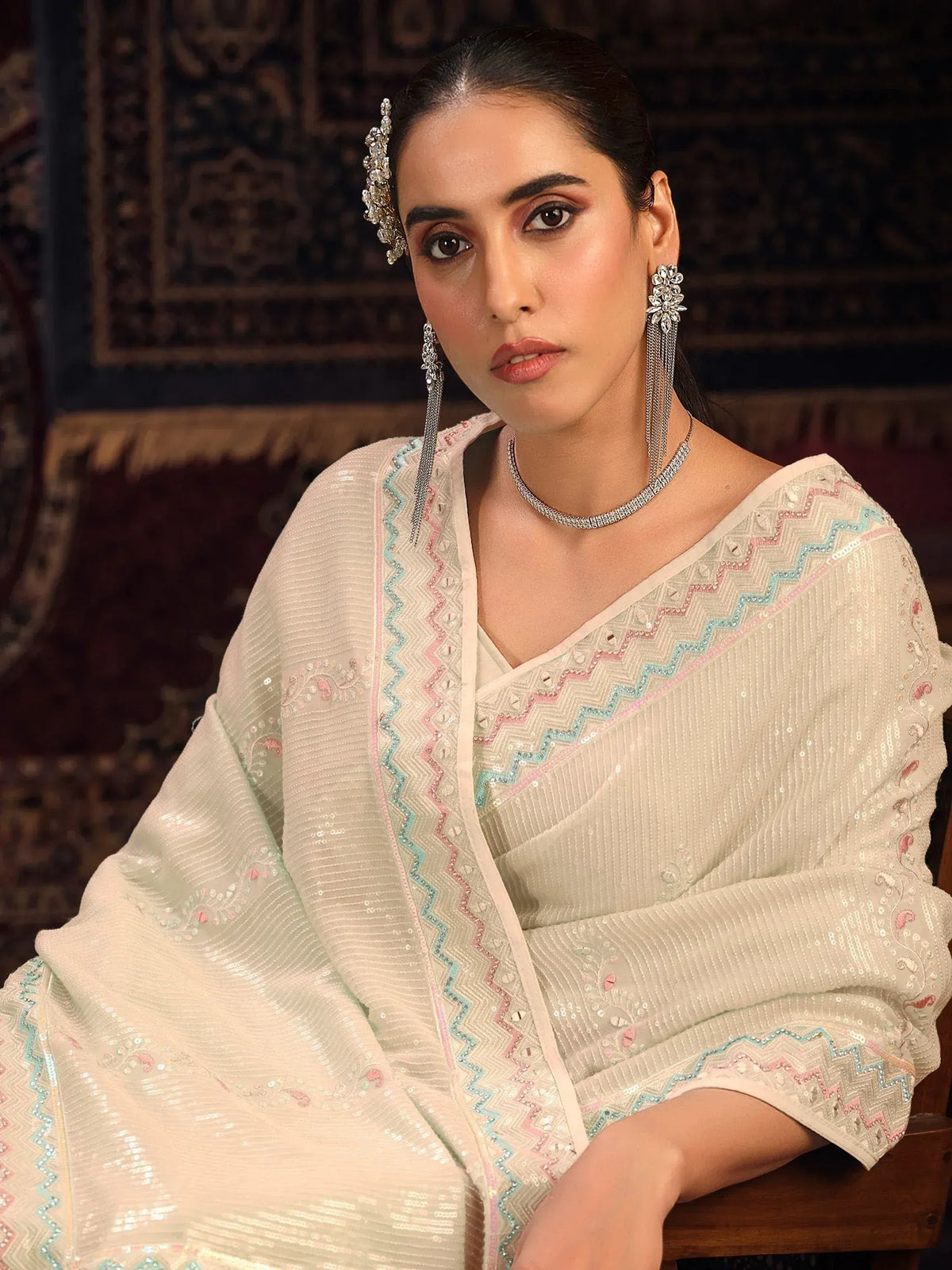 Elegant woman in cream ethnic gown with pastel embroidery, paired with statement jewelry for festive occasions.