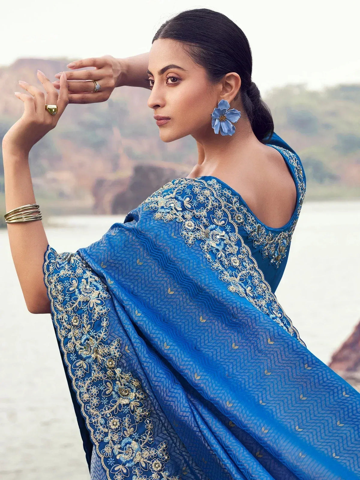 Blue embroidered saree with gold floral work, styled with statement earrings and rings, perfect for ethnic occasions.