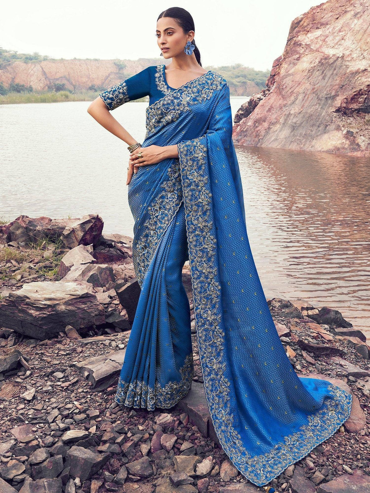 Blue embroidered saree with gold detailing, styled for ethnic occasions near a lakeside