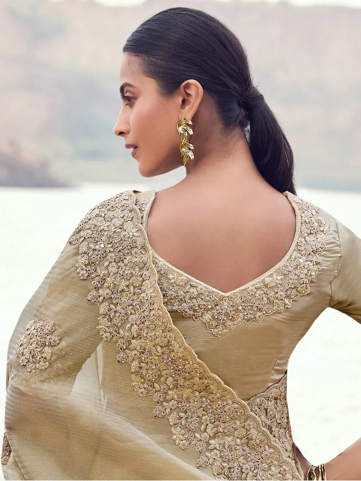 Elegant beige saree with intricate gold embroidery and leaf-style earrings, perfect for ethnic occasions.