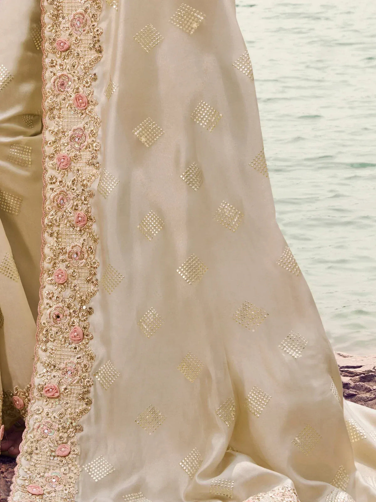 Cream ethnic gown with gold diamond embroidery and pink floral border, perfect for Indian weddings.