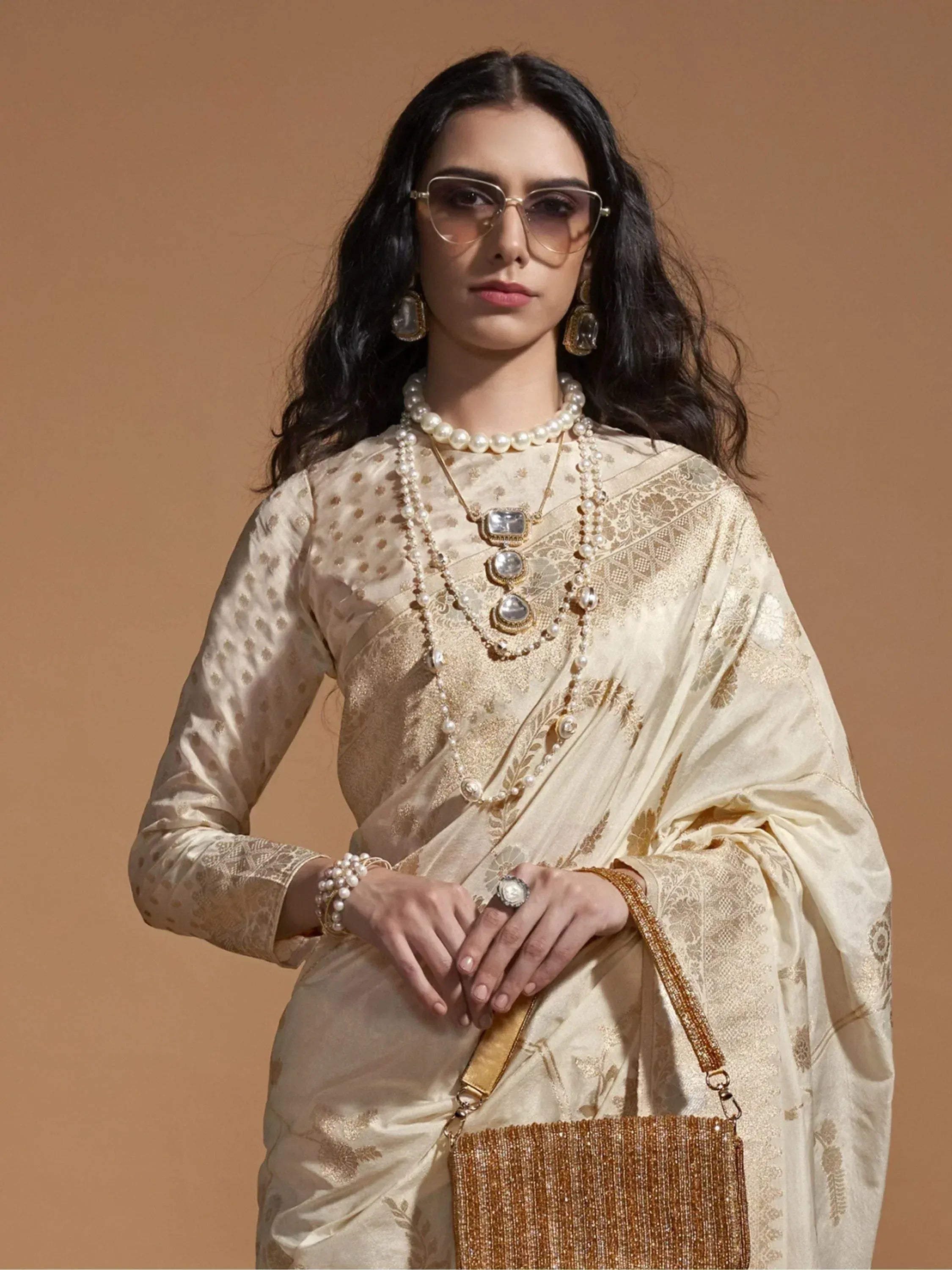 Elegant cream saree with gold embroidery, pearl jewelry, and statement sunglasses for Indian ethnic wear.