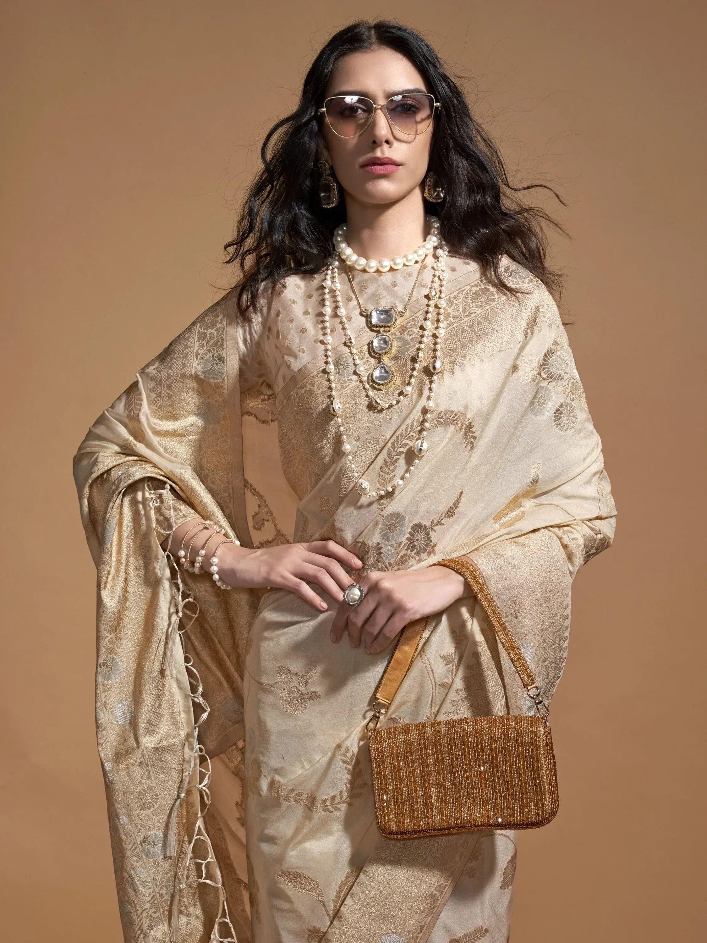 Elegant woman in gold floral saree with pearl jewelry and sunglasses, holding beaded clutch