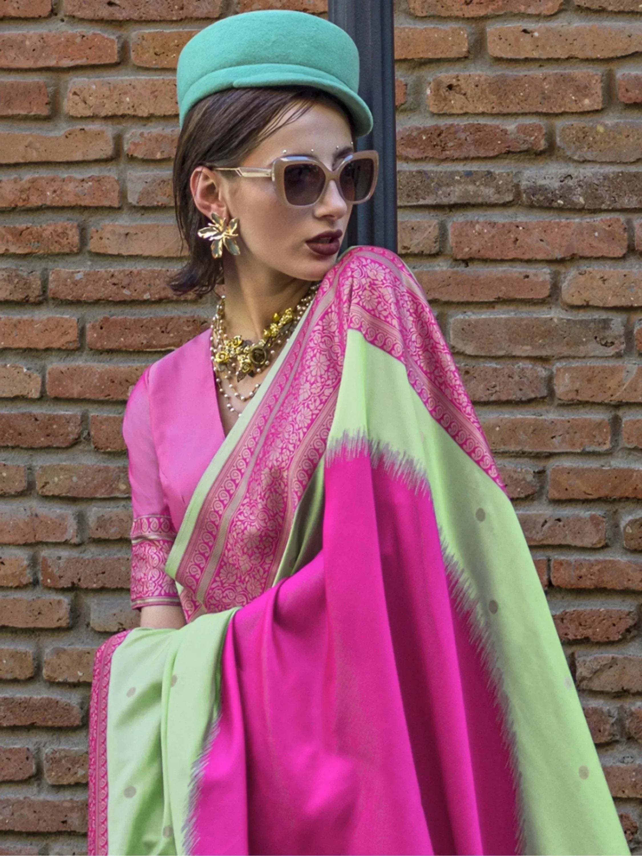 Woman in vibrant pink and green saree with gold jewelry and mint hat, styled for ethnic fashion