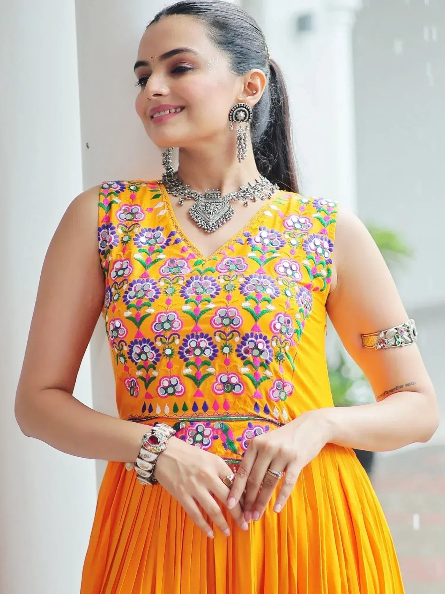 Vibrant yellow ethnic gown with floral mirror embroidery, paired with traditional jewelry for festive occasions