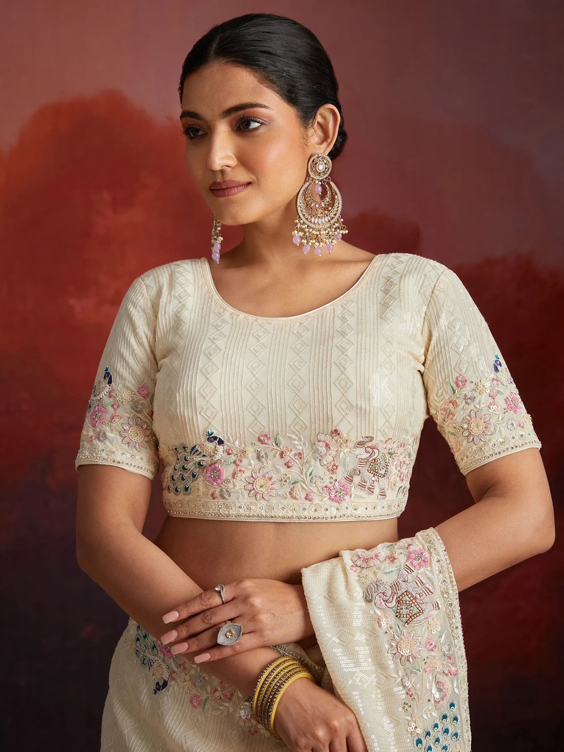 Cream embroidered lehenga choli with floral and peacock motifs, paired with statement earrings for Indian ethnic wear.