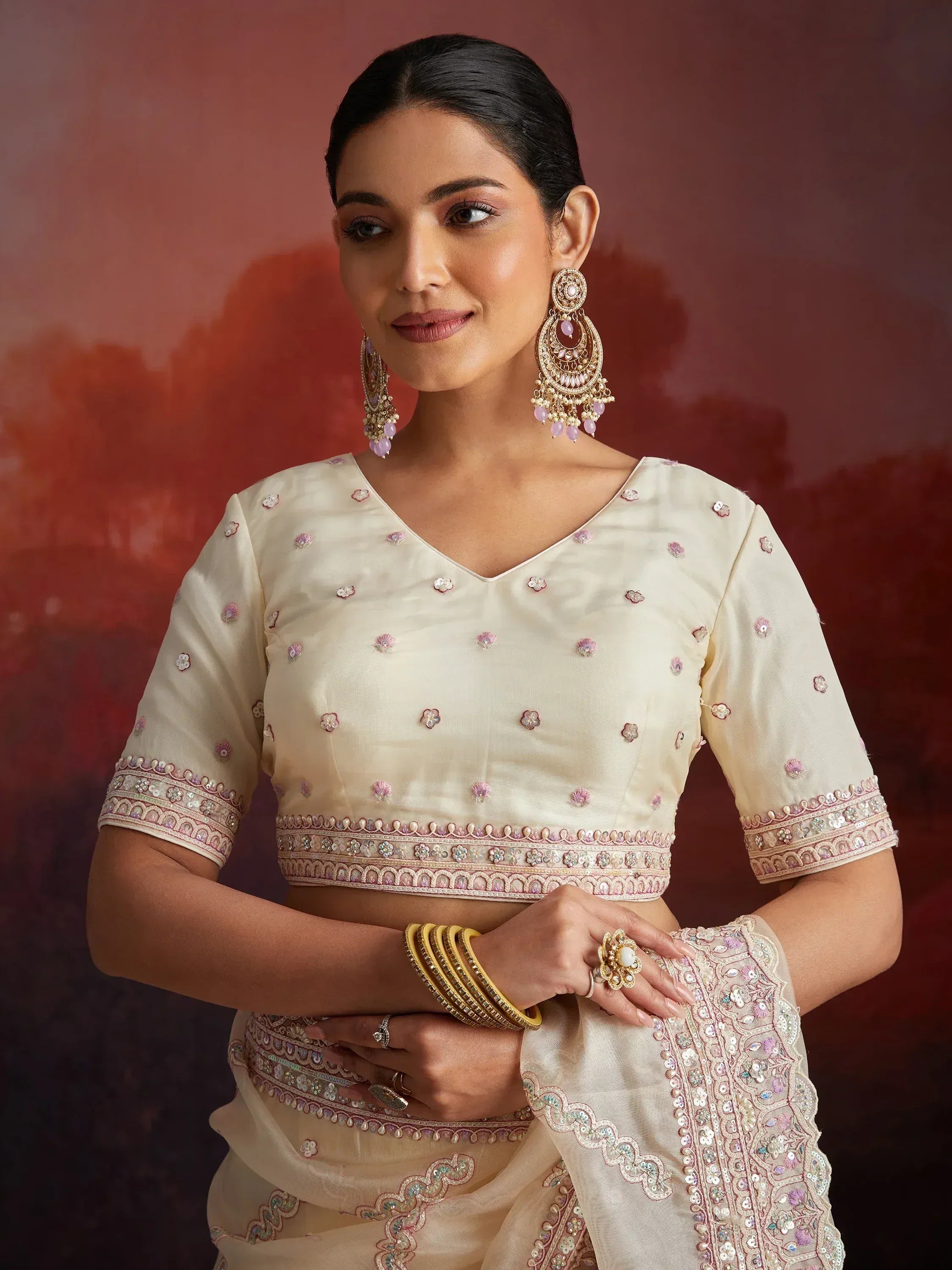 Elegant cream saree with pink floral embroidery and matching blouse, styled with gold jewelry for Indian ethnic wear.