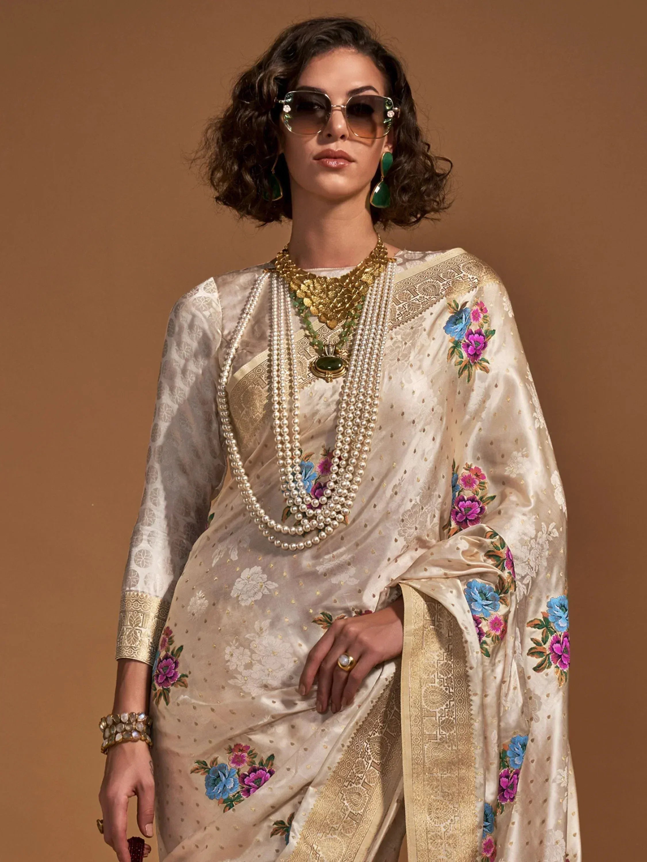 Elegant cream saree with floral embroidery and gold border, paired with pearl necklace and statement earrings.