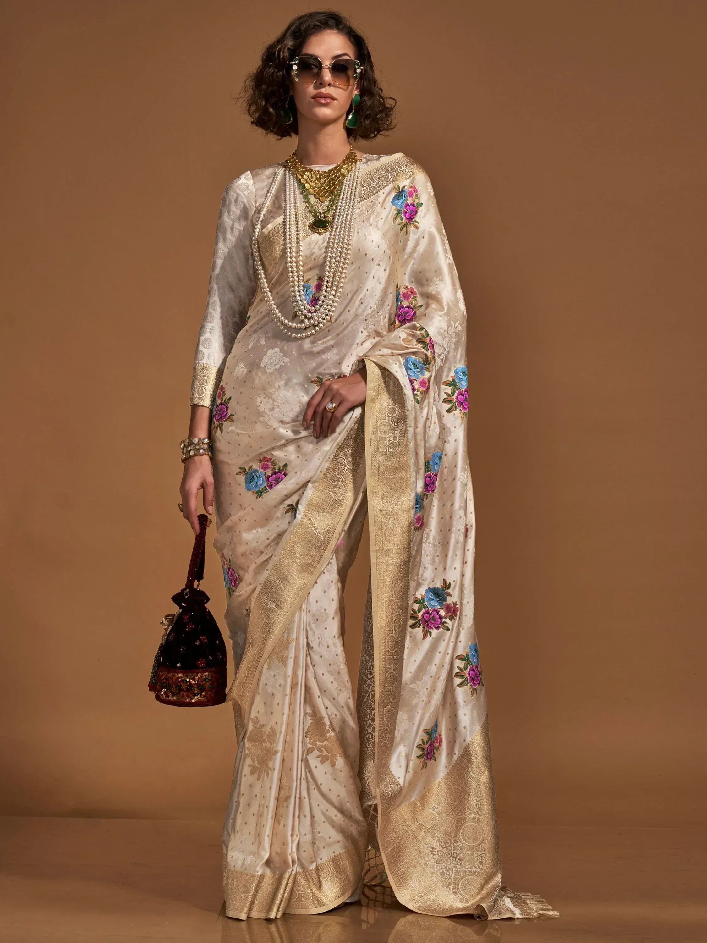 Cream floral embroidered saree with gold border, styled with pearls and statement jewelry for Indian ethnic wear.