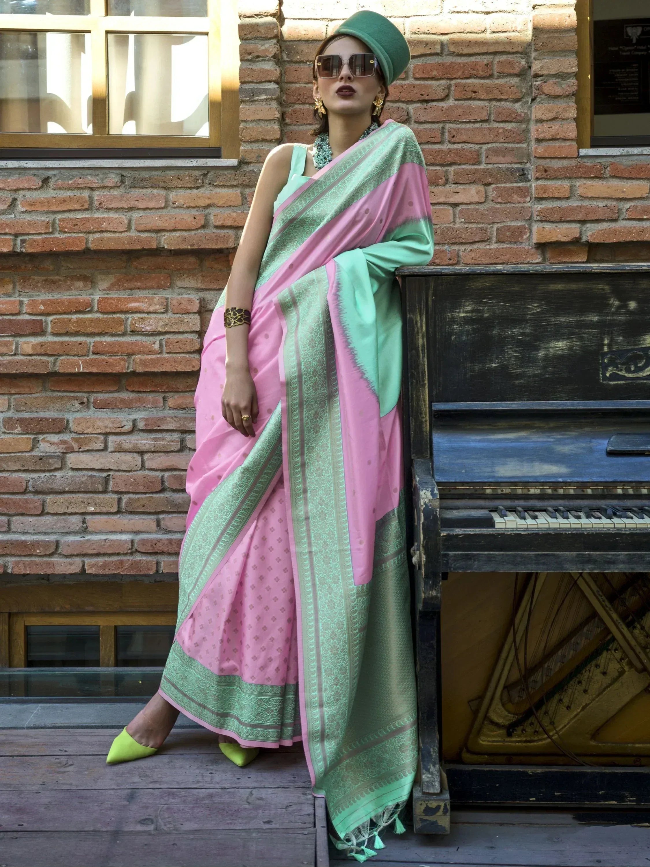 Pink and mint green designer saree with gold border, styled with green hat and heels, perfect for ethnic occasions.